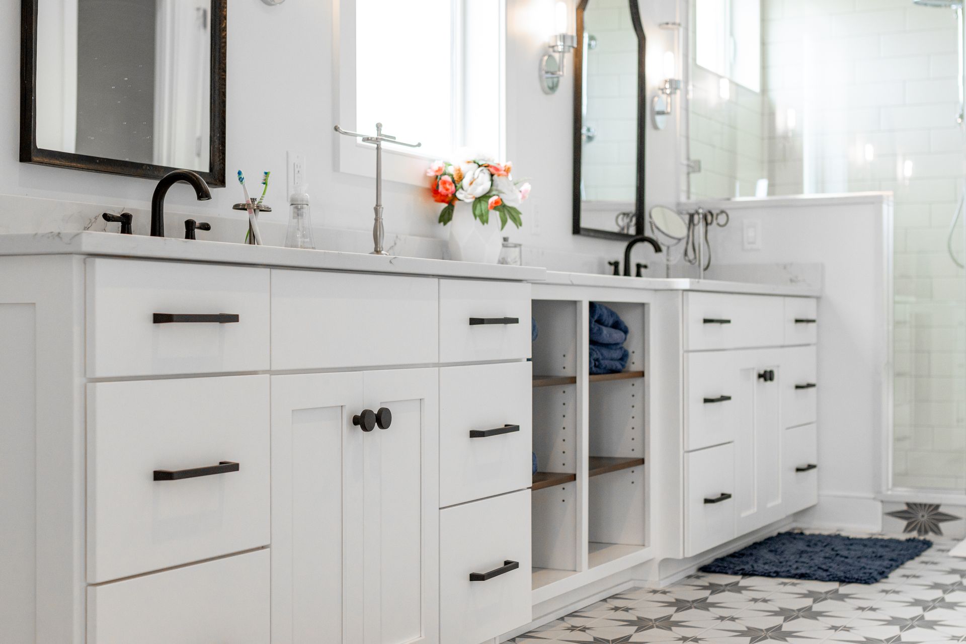 White bathroom vanity with black hardware, sinks, and mirrors. Flower arrangement.