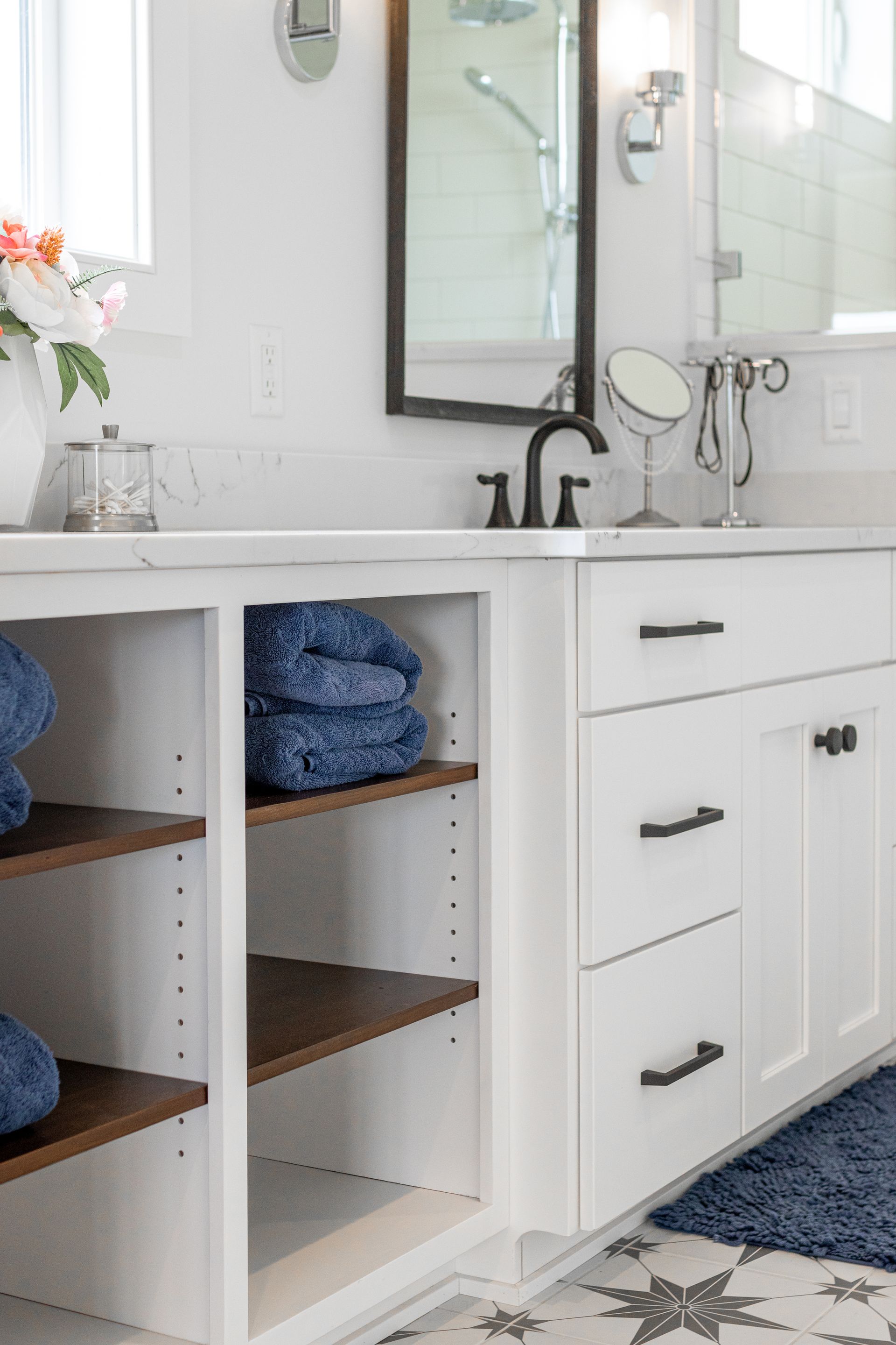 White bathroom vanity with open shelves holding blue towels, and closed drawers/doors.