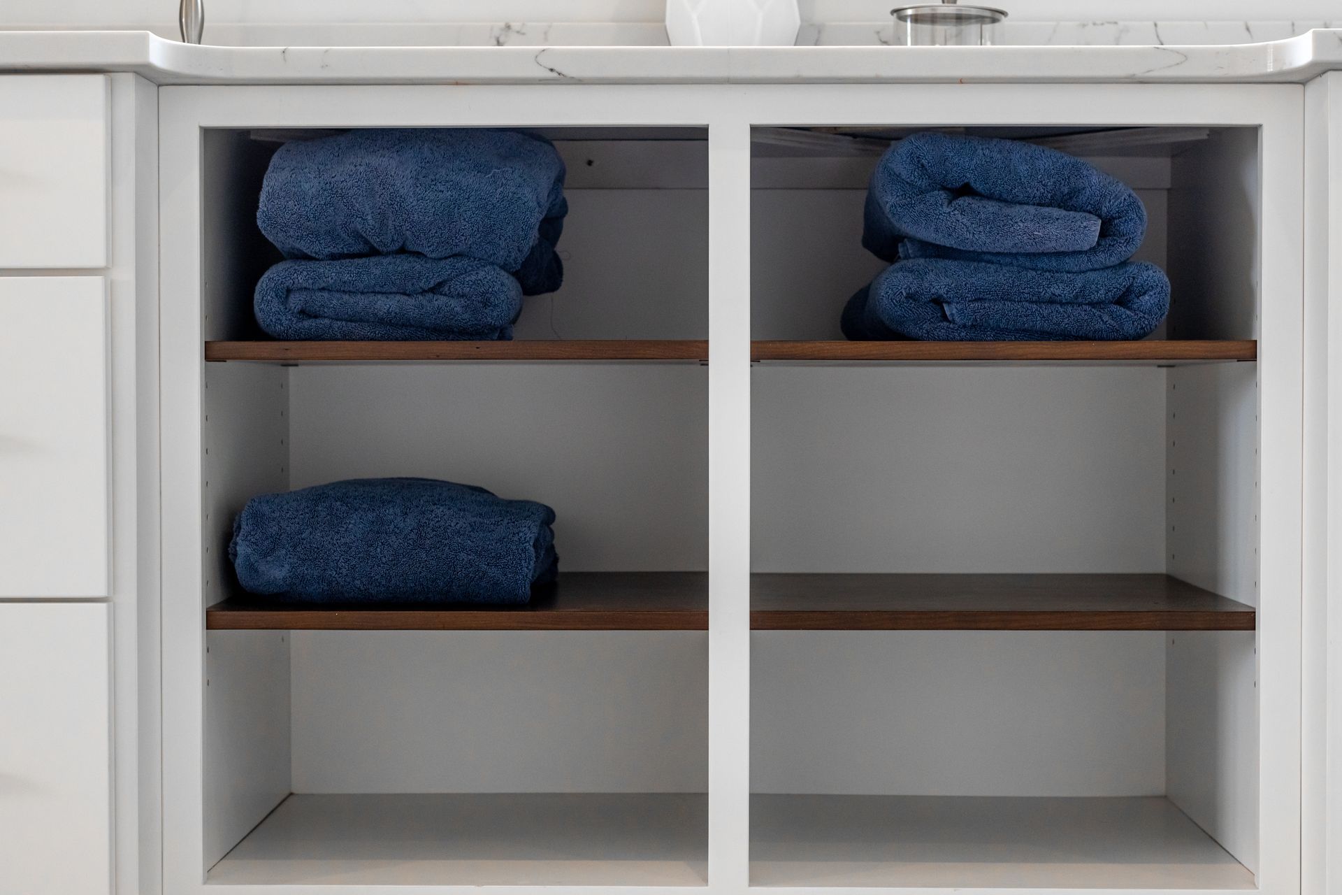 White bathroom cabinet with open shelves, holding folded blue towels.