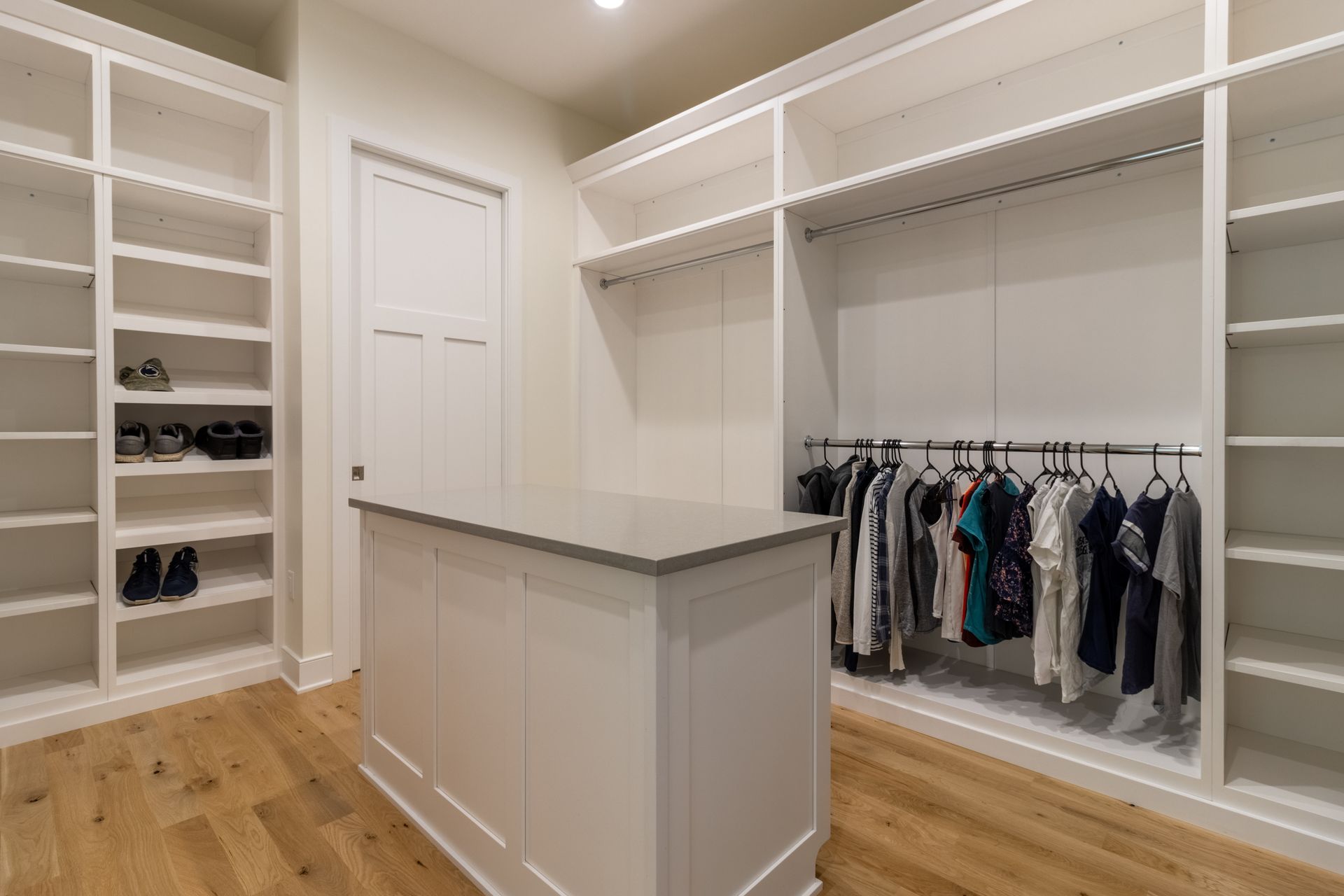 Walk-in closet with white shelving, hanging clothes, and a central island with a grey countertop.