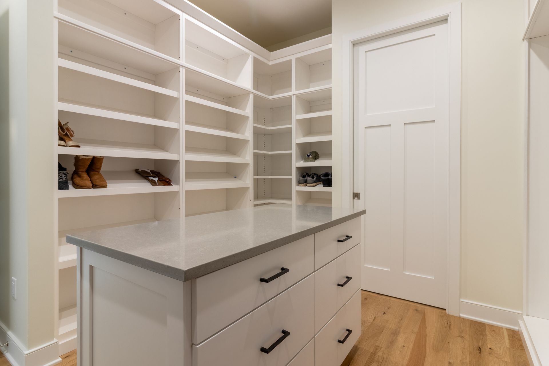 White walk-in closet with built-in shelving and a center island with drawers, light wood floor, and white door.