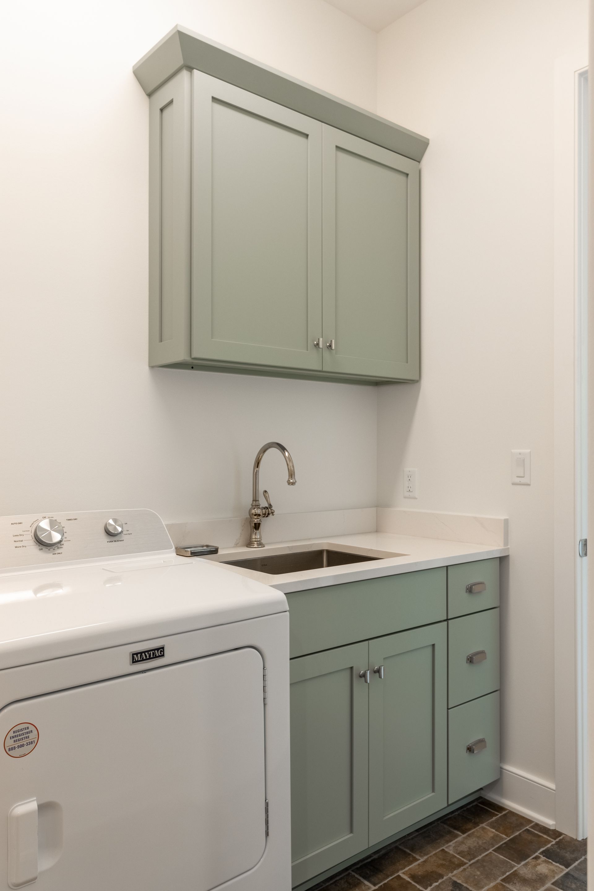 Laundry room with a washing machine, sink, and green cabinets.