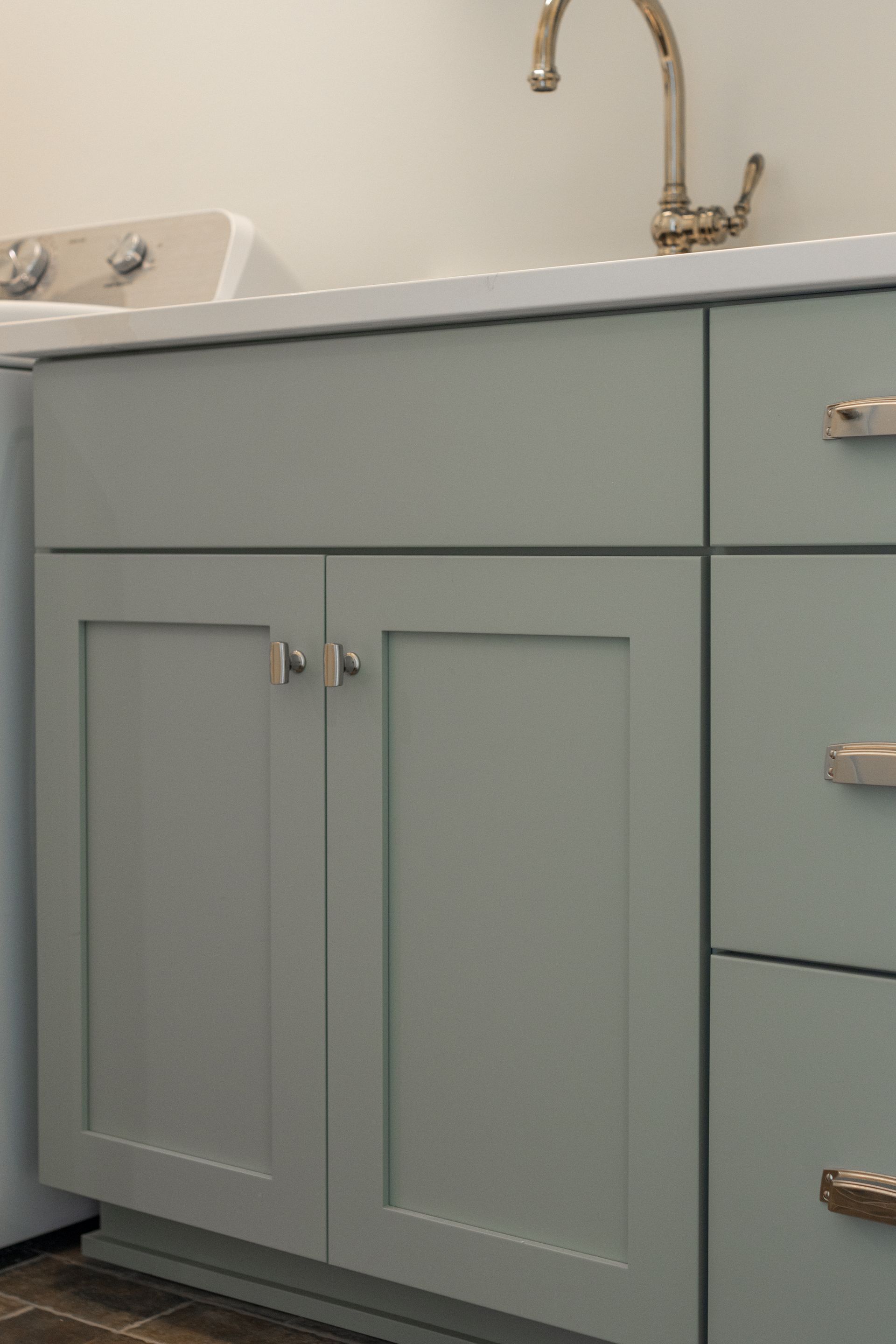 Light green laundry room cabinets with silver hardware and a white countertop.