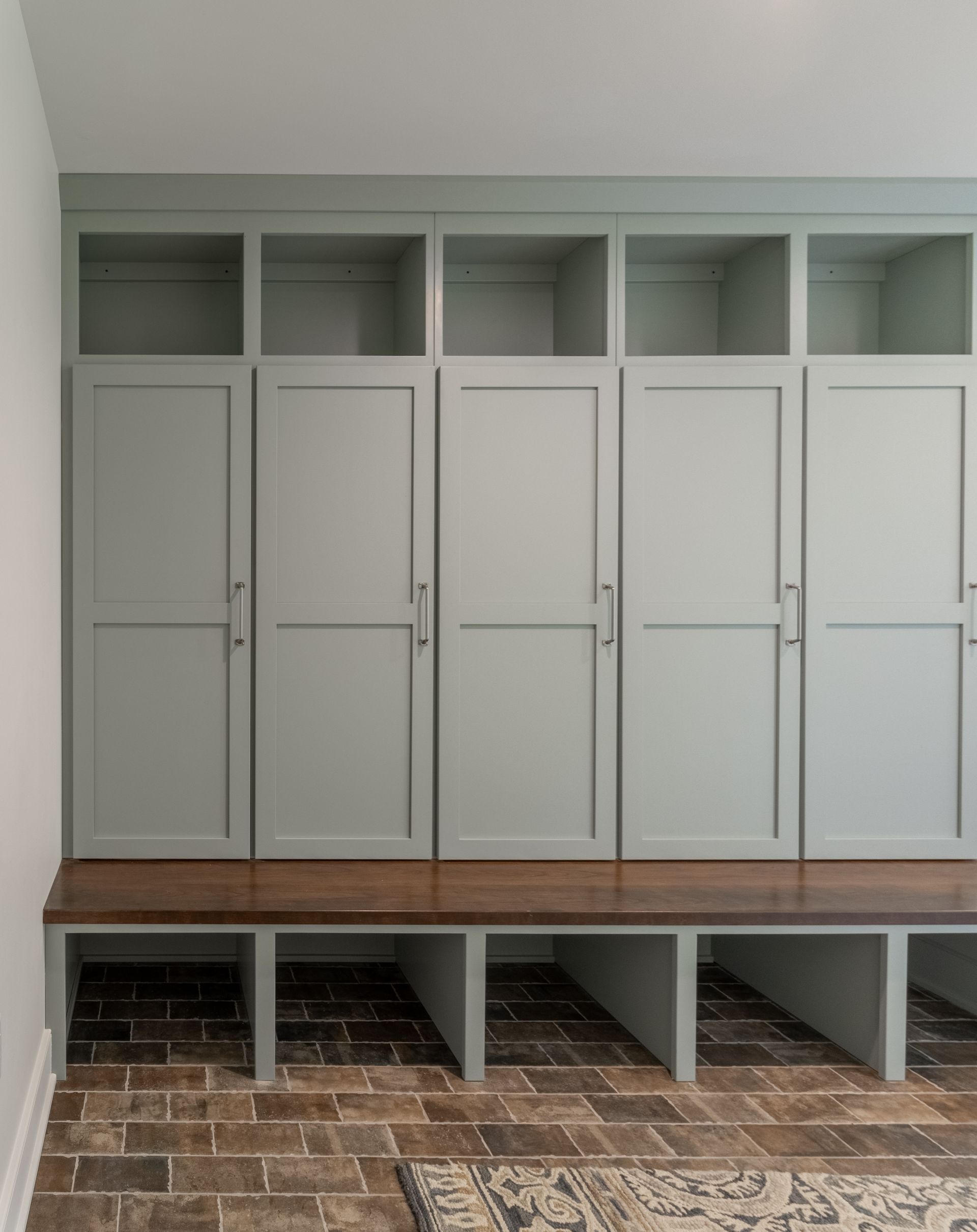 Built-in storage unit with open top shelves, closed doors, and bench seating, painted light green; over brick flooring.