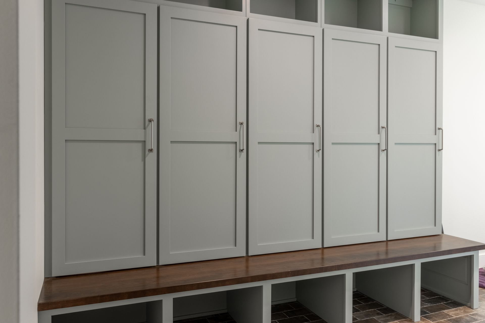 Gray cabinets with a wood bench and open cubbies below.