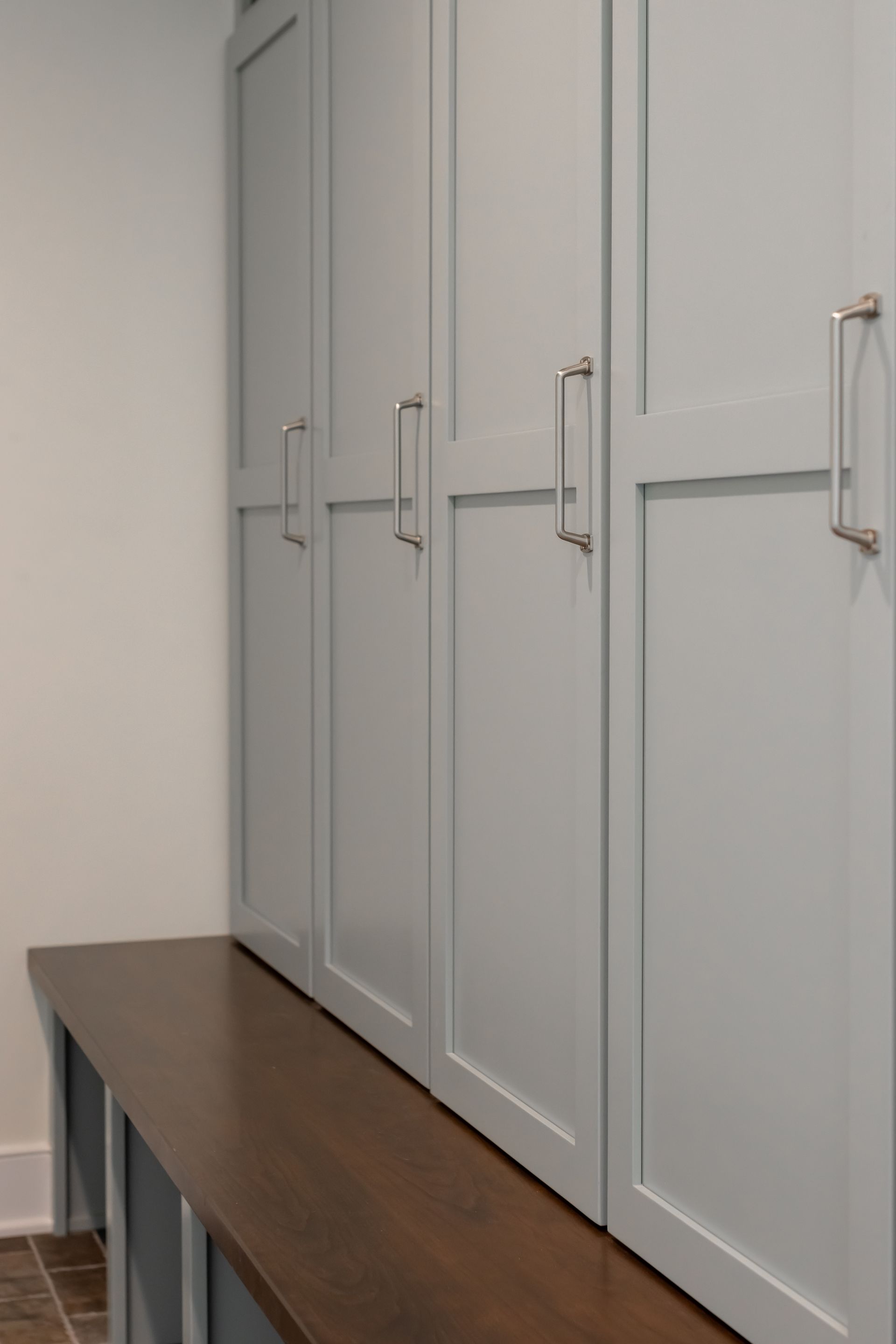Blue storage cabinets with silver handles above a brown bench.