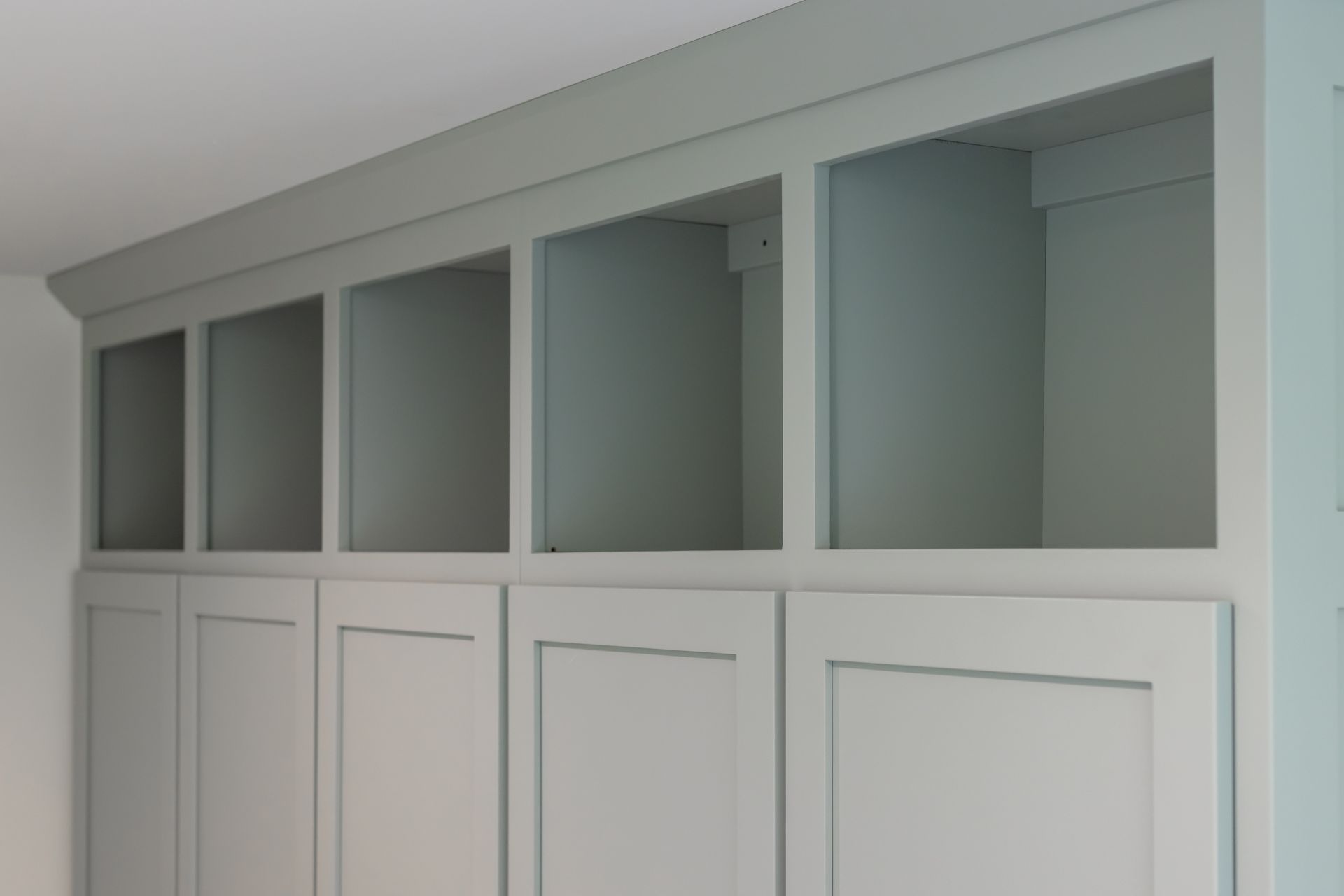 Built-in cabinetry with open shelving above paneled cabinet doors, all painted light blue-gray.