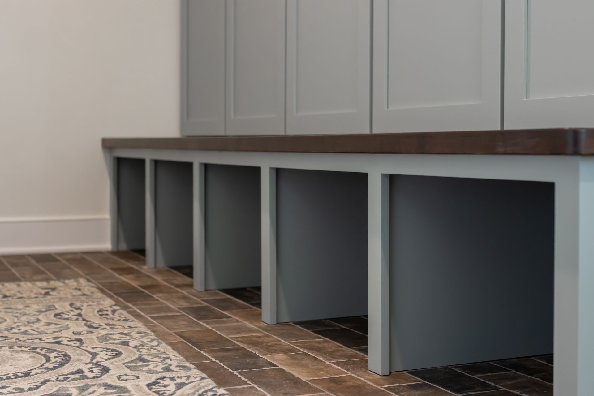 Built-in bench with cubbies below, next to gray cabinets, on wood-look tile floor.