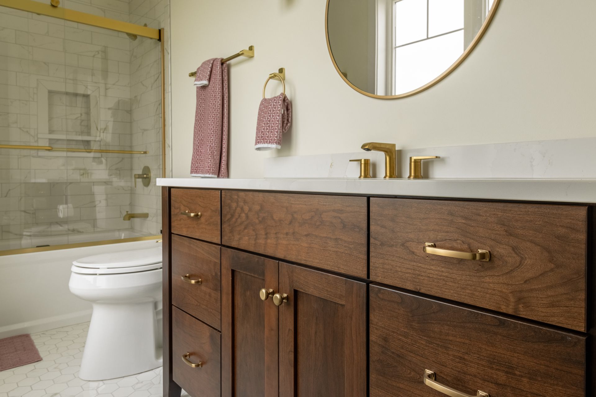 Bathroom with dark wood vanity, gold fixtures, and a round mirror.