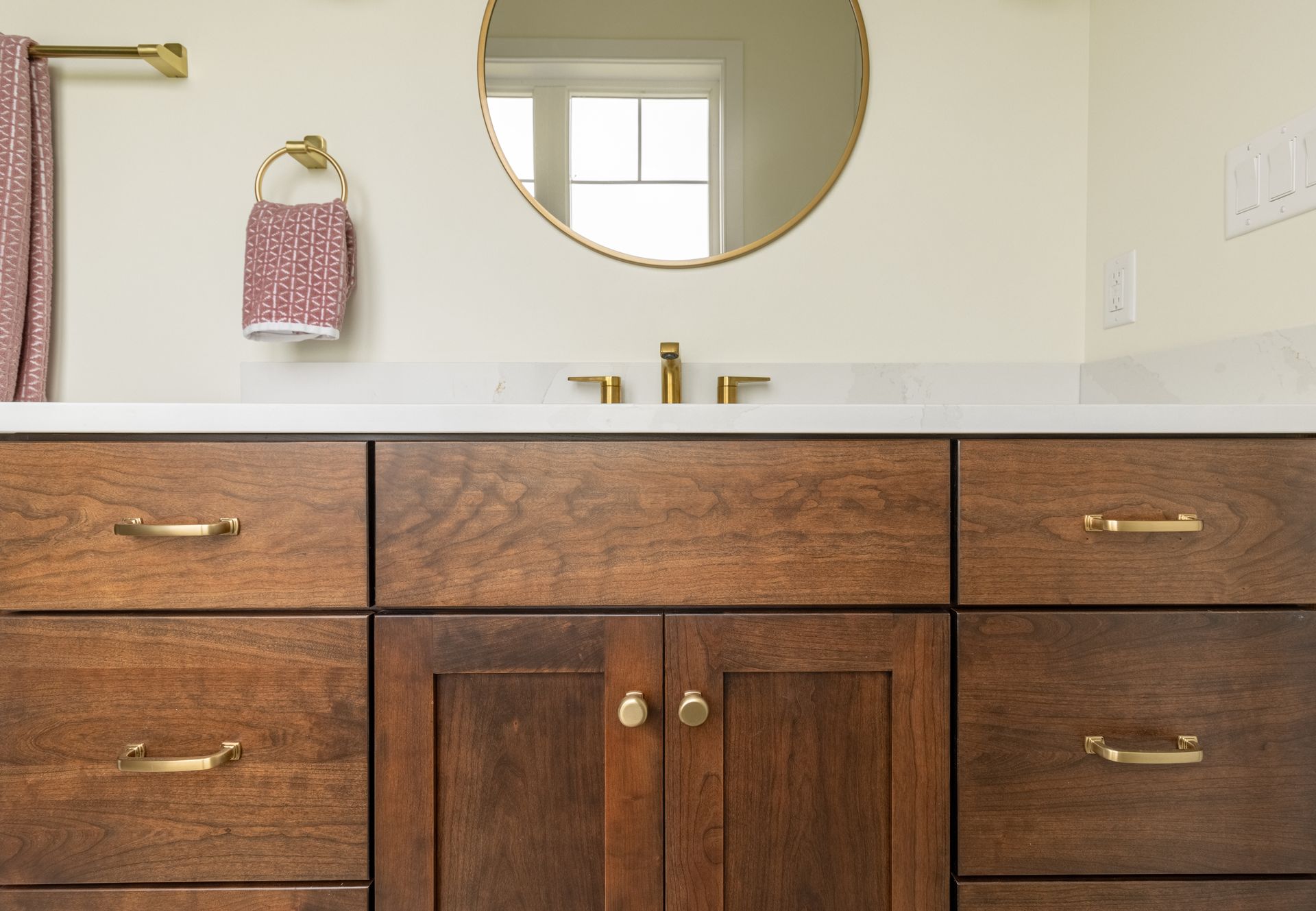 Wooden bathroom vanity with gold hardware, a round mirror, and a patterned towel.