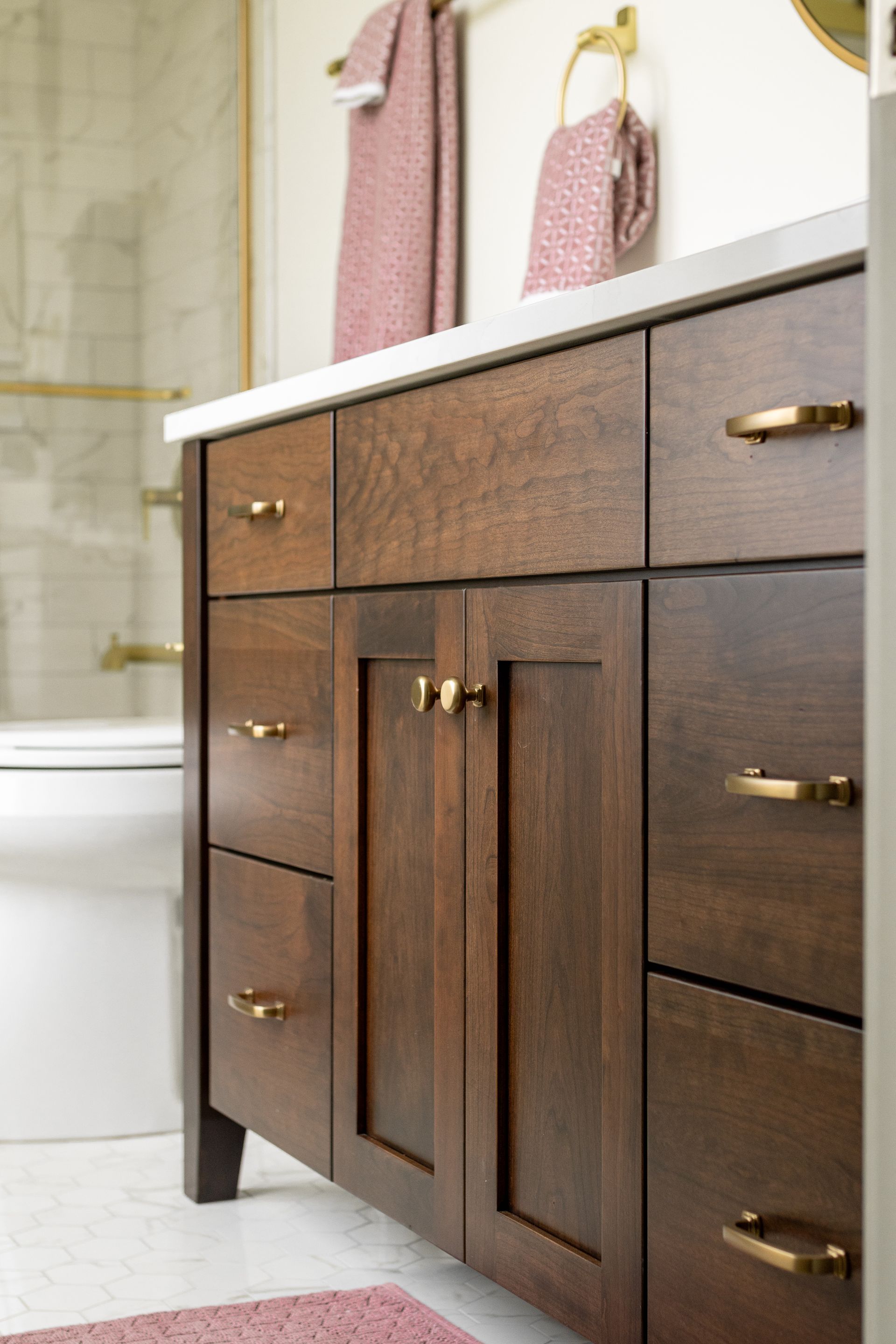 Dark wood bathroom vanity with gold hardware, white countertop, and pink towels.