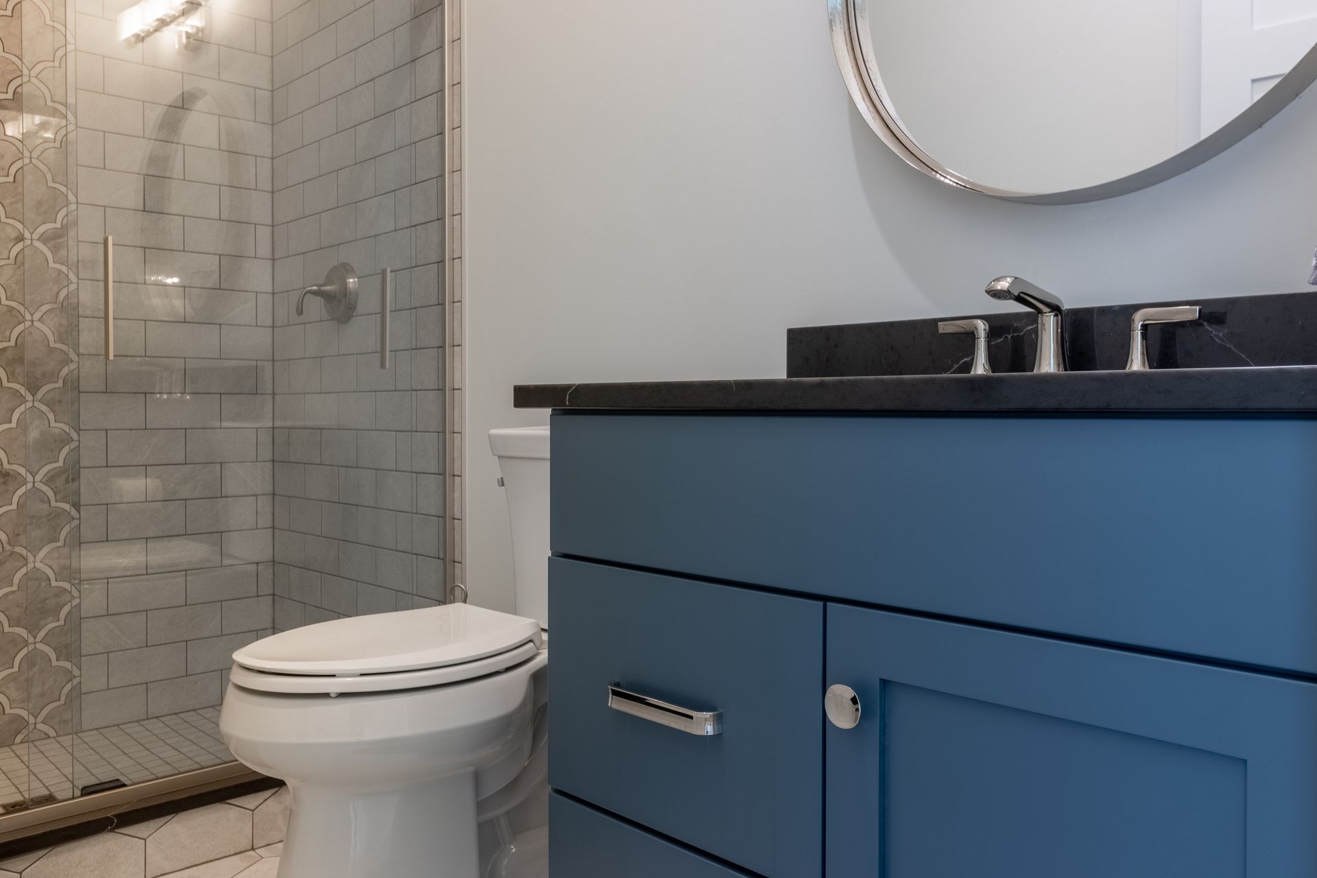 Blue vanity with black countertop in a bathroom. Toilet, shower stall, and mirror are visible.
