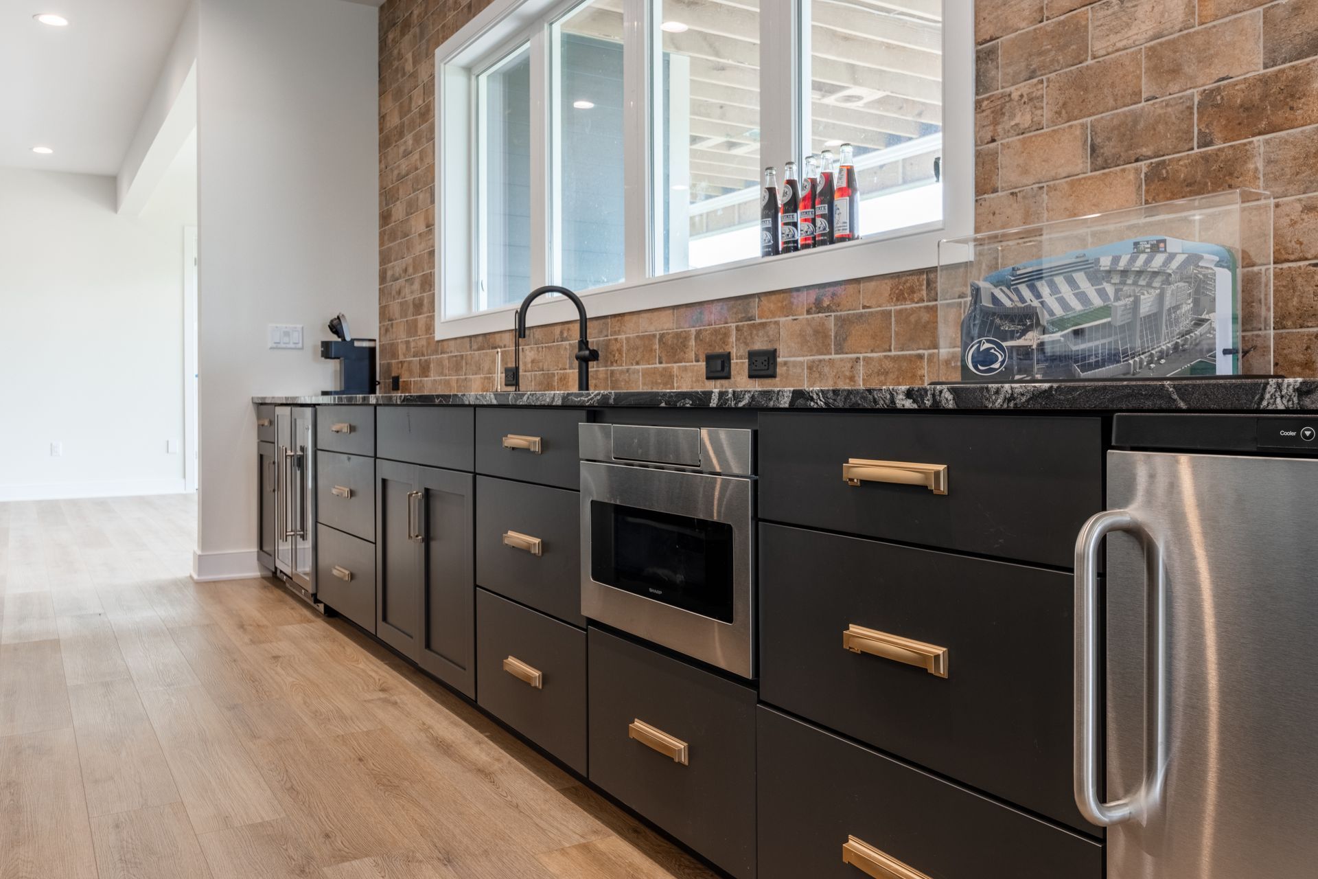 Dark gray kitchen cabinets with gold hardware, stainless steel appliances, and a brick backsplash.
