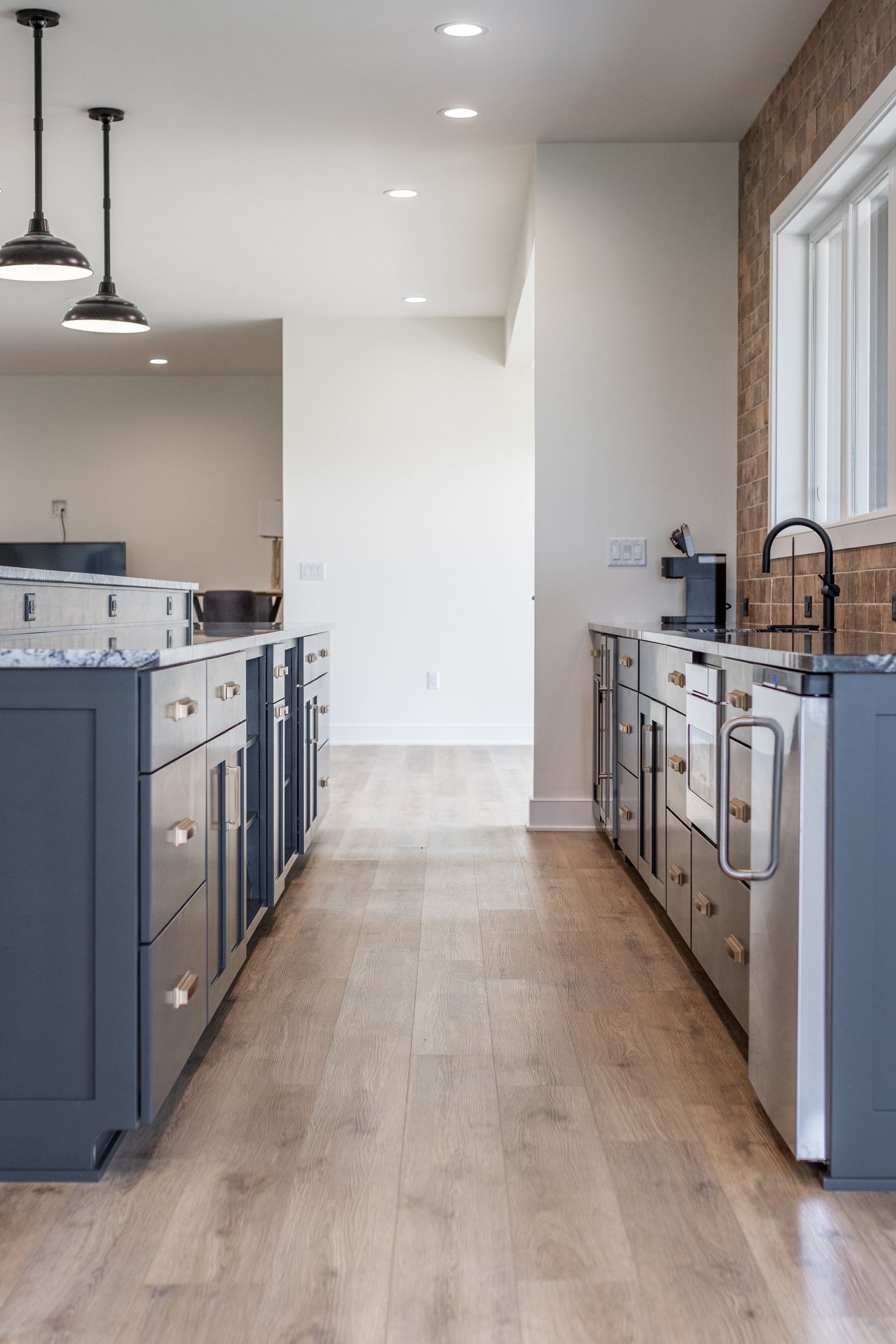 Modern kitchen with two dark blue islands, light wood floor, and white walls.