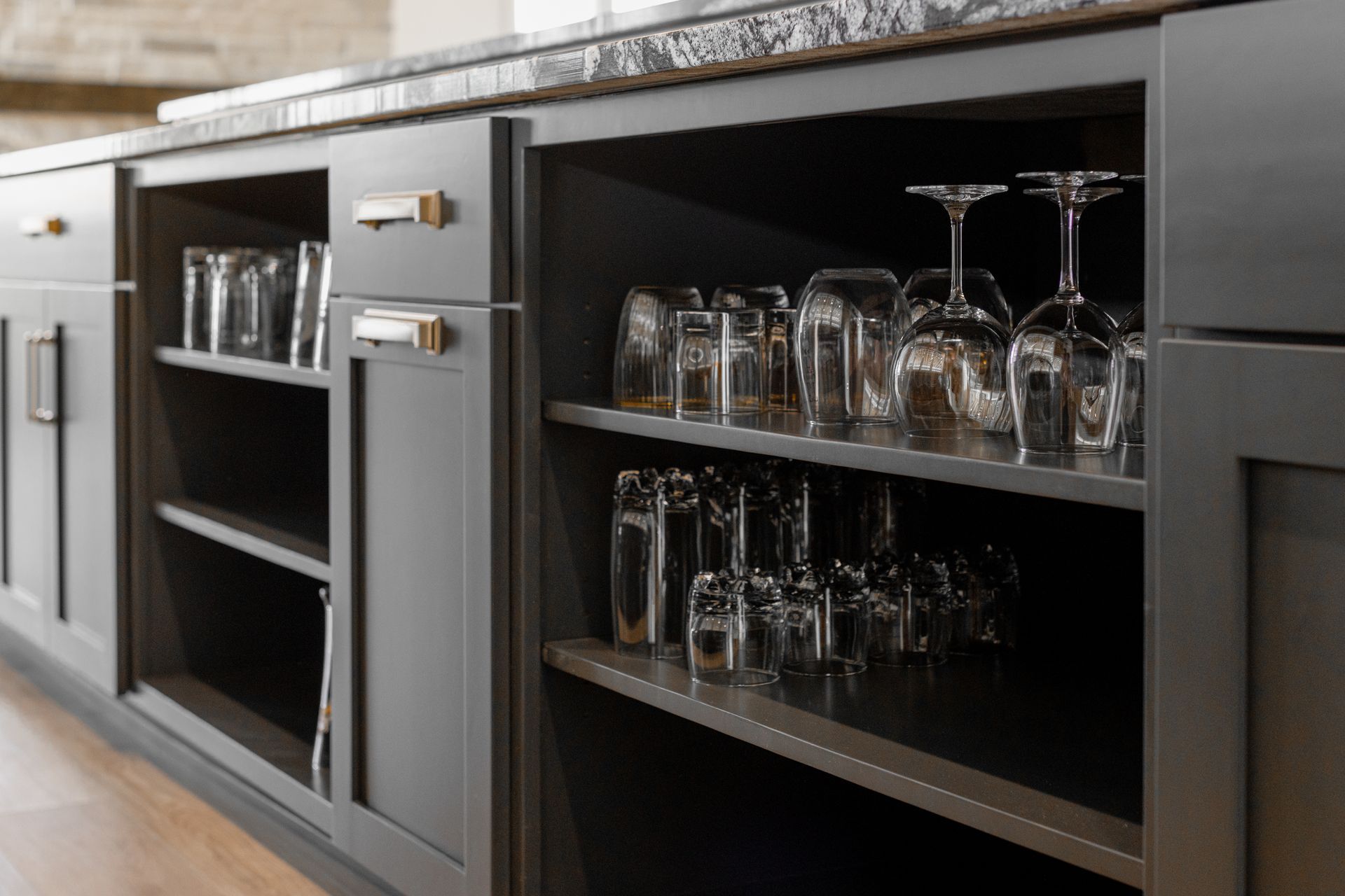 Dark gray cabinets with open shelves holding glassware under a countertop.