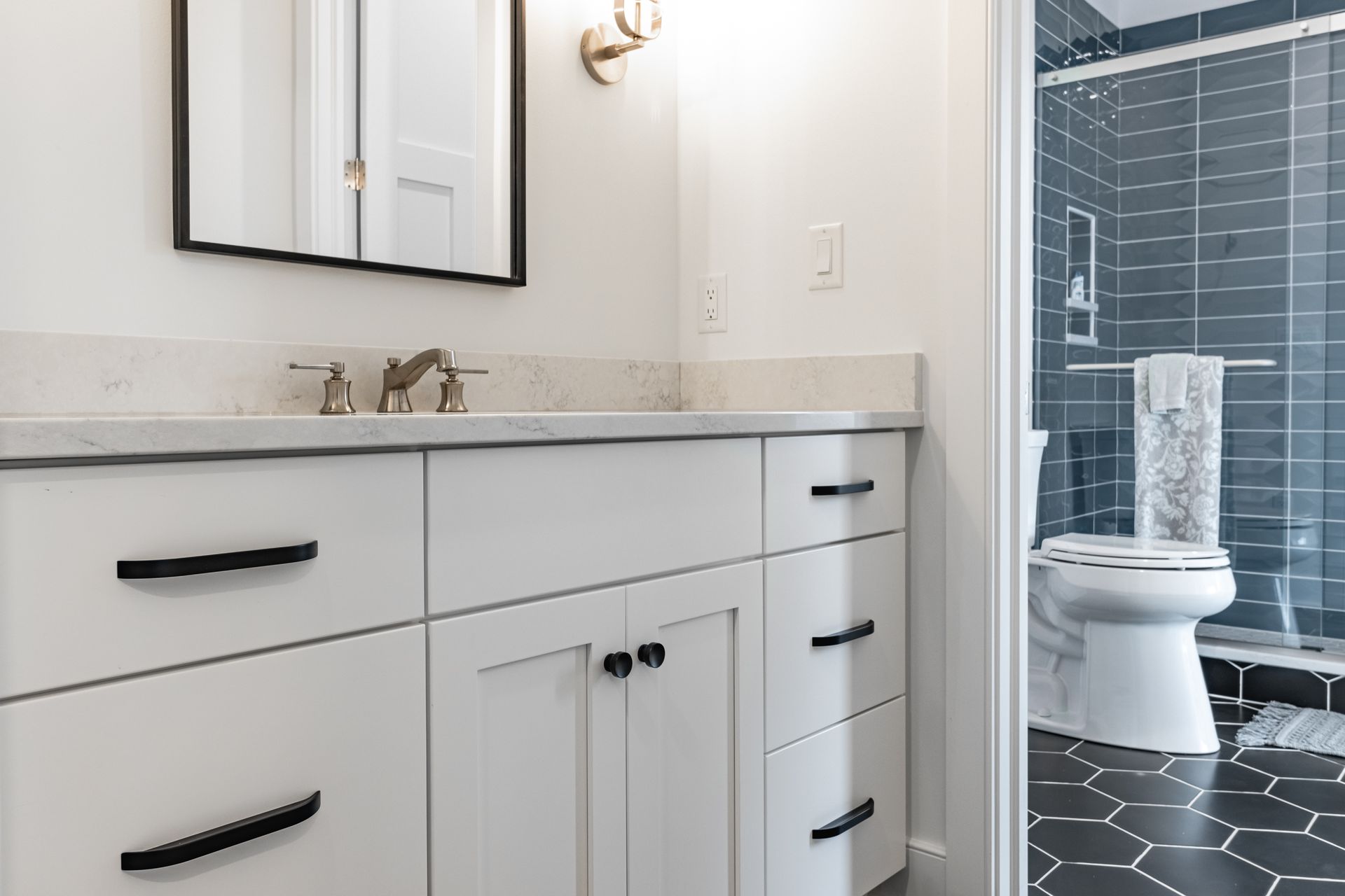 Bathroom with white vanity, black hardware, gray countertop, and a dark blue tiled shower.
