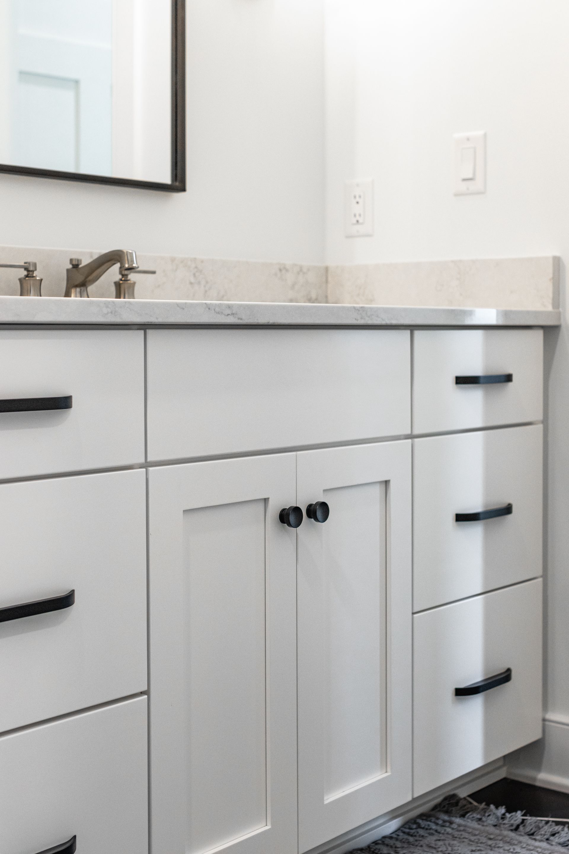 White bathroom vanity with black hardware, marble countertop, and mirror.