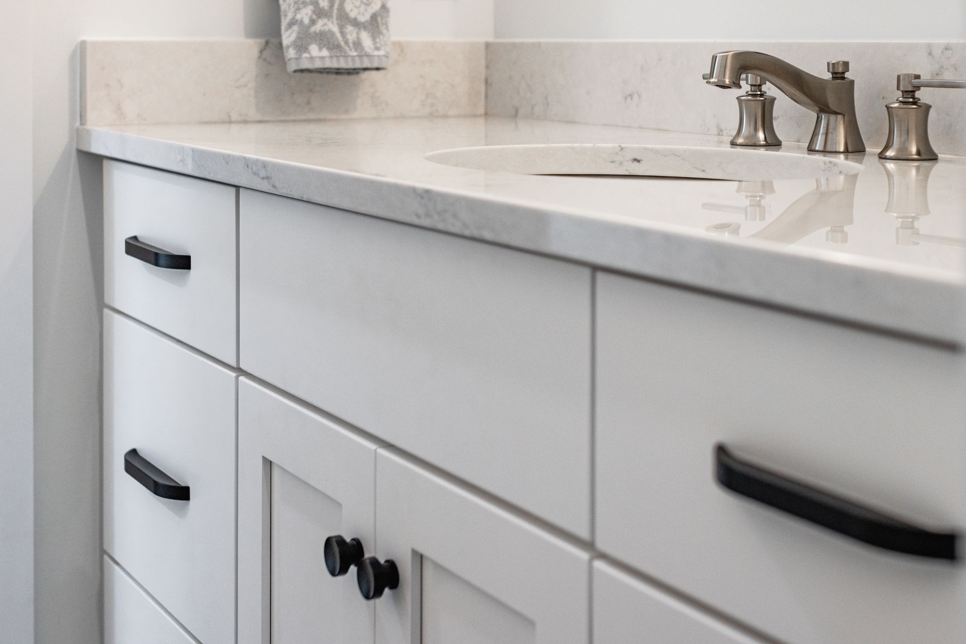 White bathroom vanity with black hardware, marble countertop, and chrome faucet.