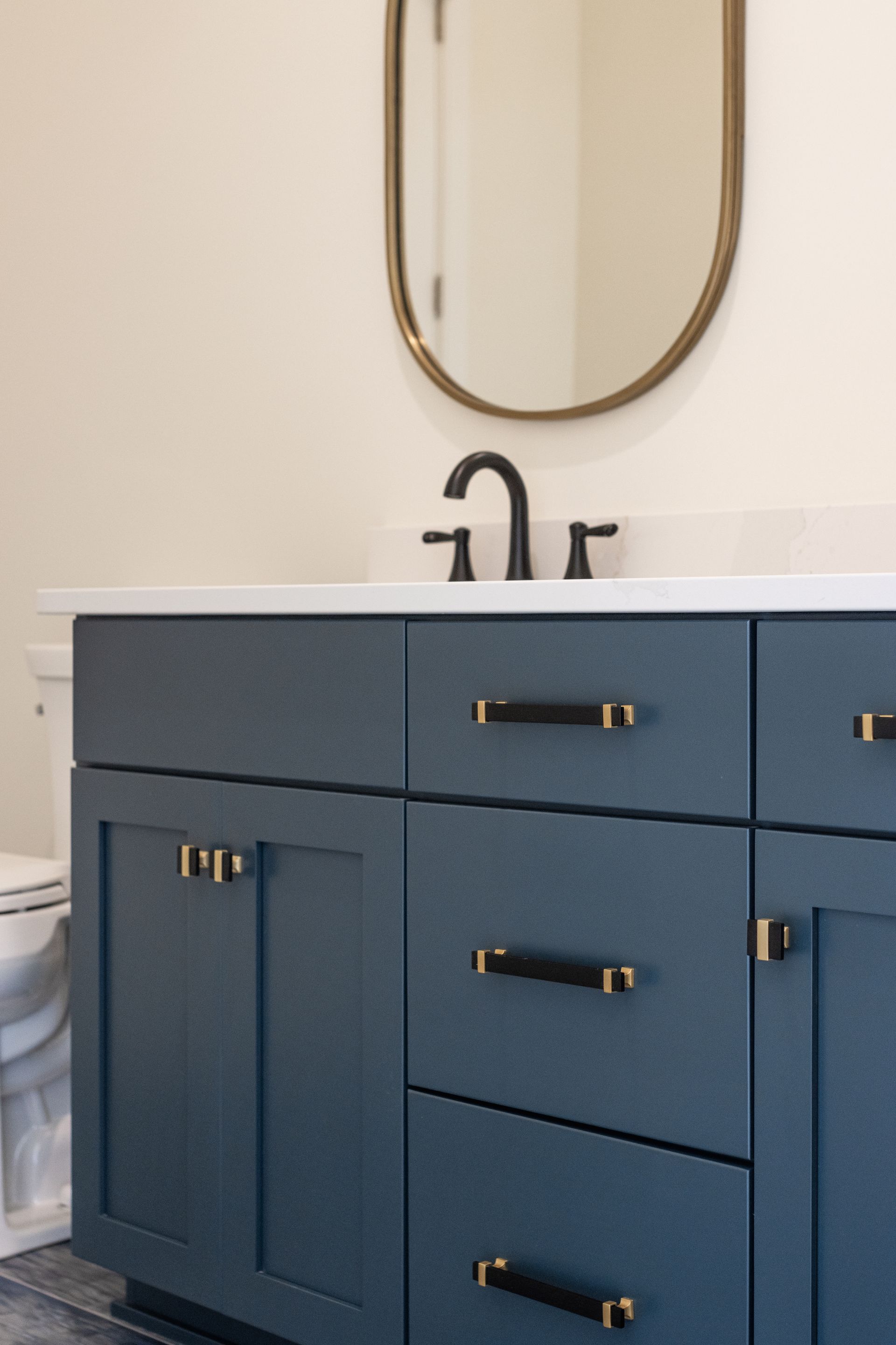 Blue bathroom vanity with black hardware, white countertop, oval mirror.
