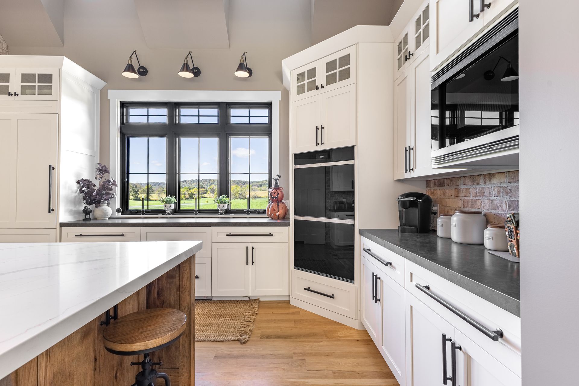 White kitchen with a black window, oven, and hardware. Wood island and floor.