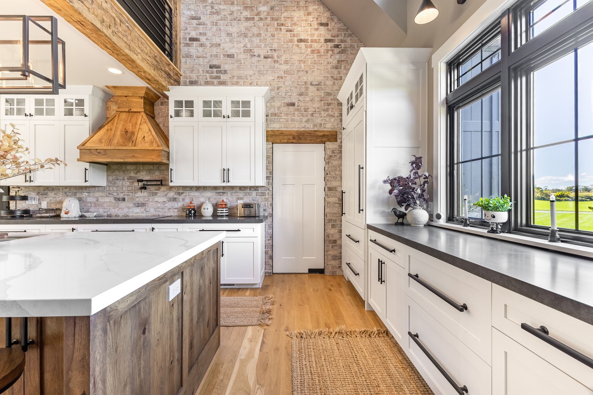 Kitchen with white cabinets, stone backsplash, wooden island, large window with black trim, and wood beams.