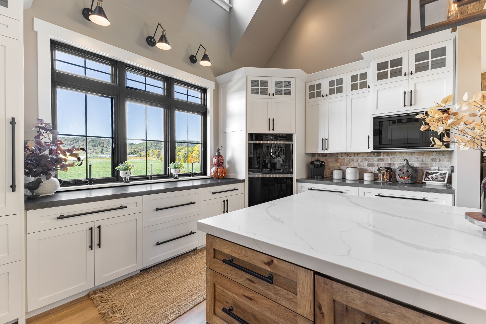 White kitchen with large window, island, and cabinets. Black accents and natural light.