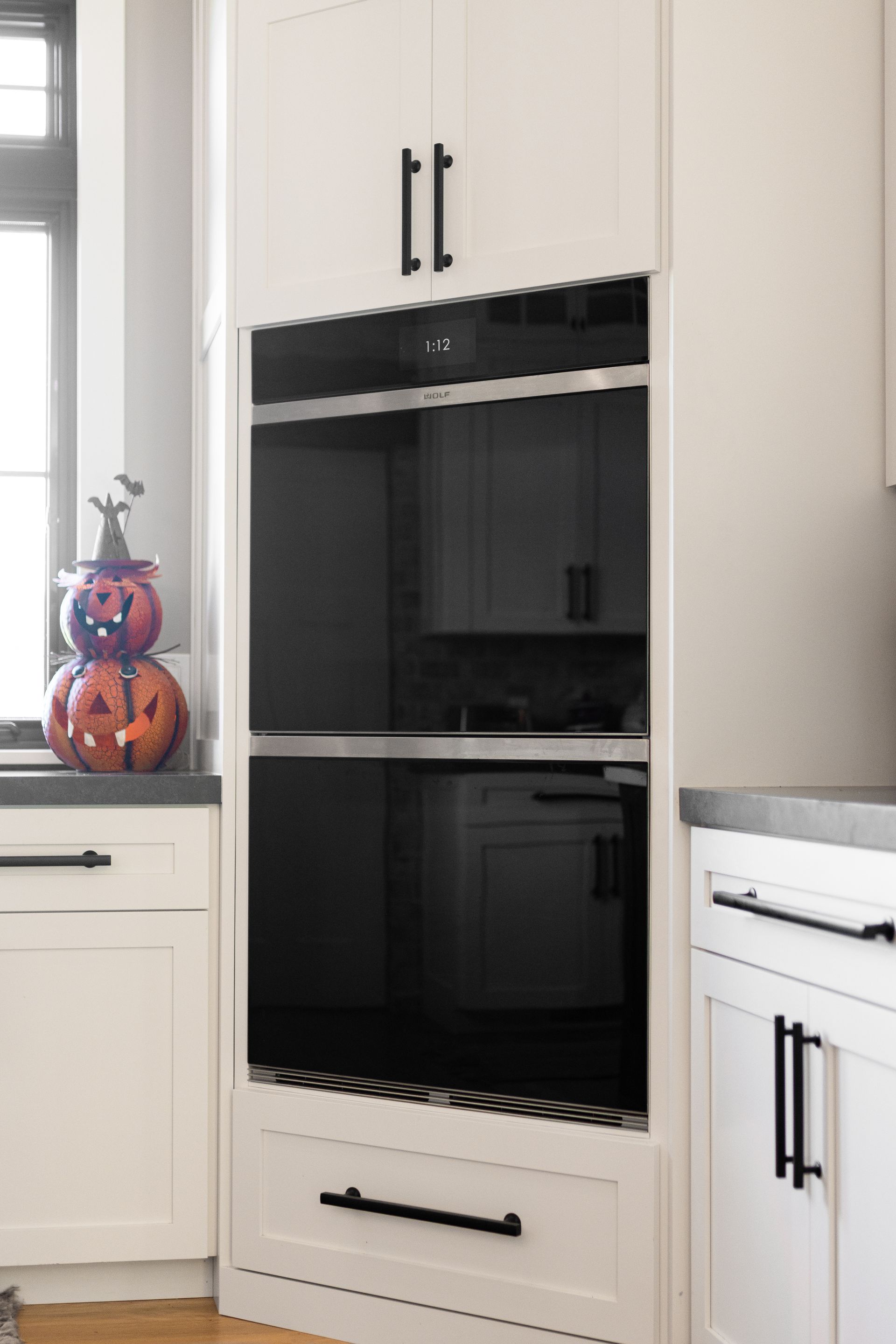 Built-in white oven with black glass door, surrounded by white cabinets with black hardware, in a kitchen.