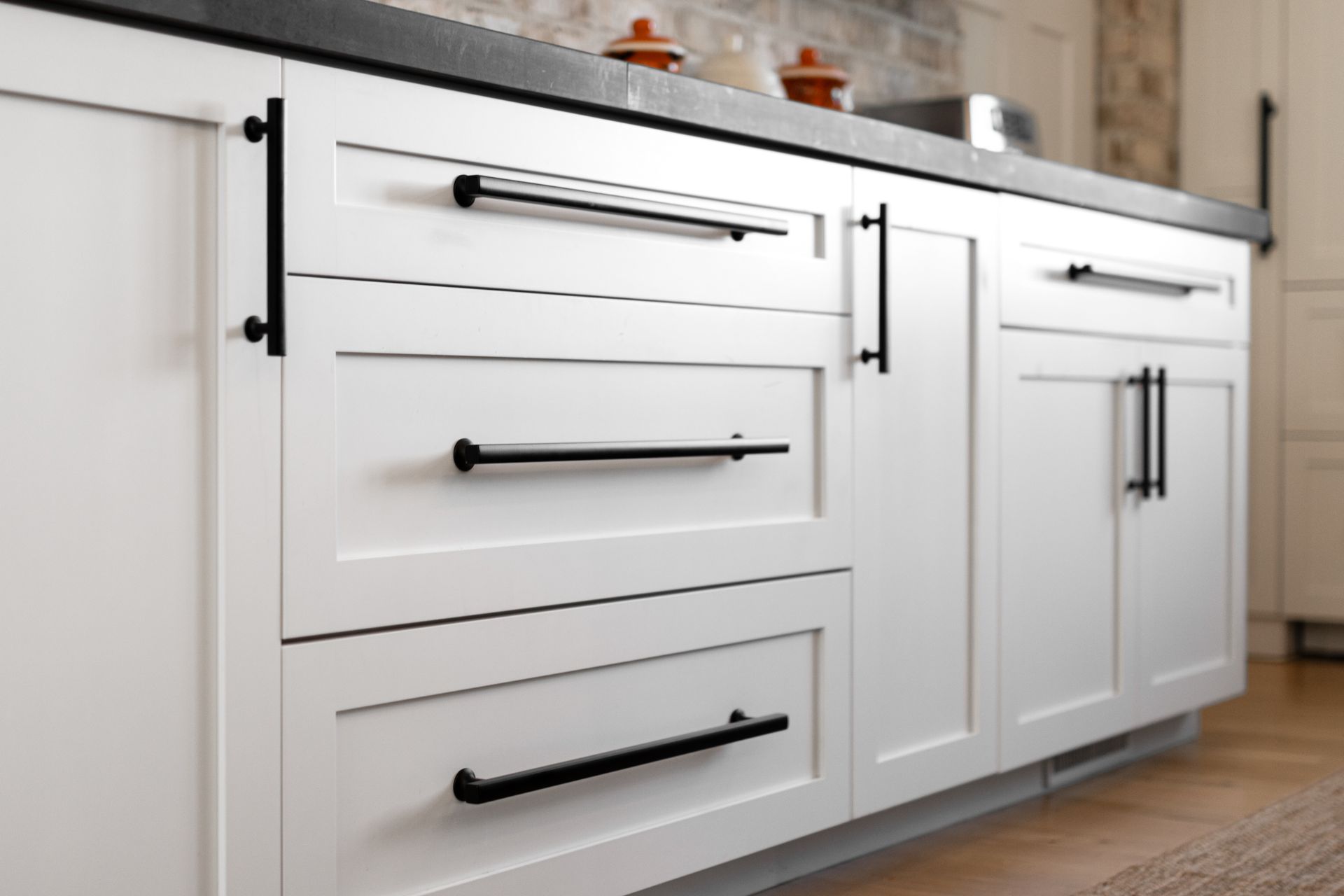White kitchen cabinets with black hardware and a dark countertop.