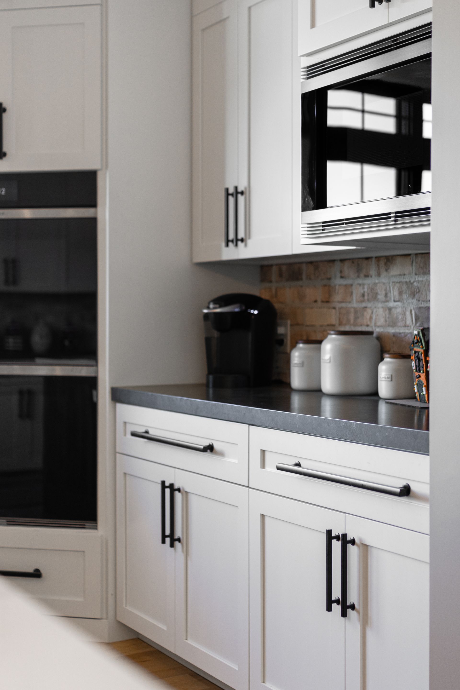 White kitchen cabinets with black hardware and appliances, dark countertop.