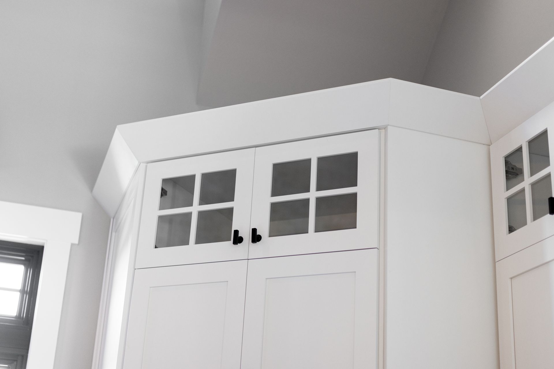 White kitchen cabinets with glass-paneled doors. Angled upper corner cabinet with crown molding.