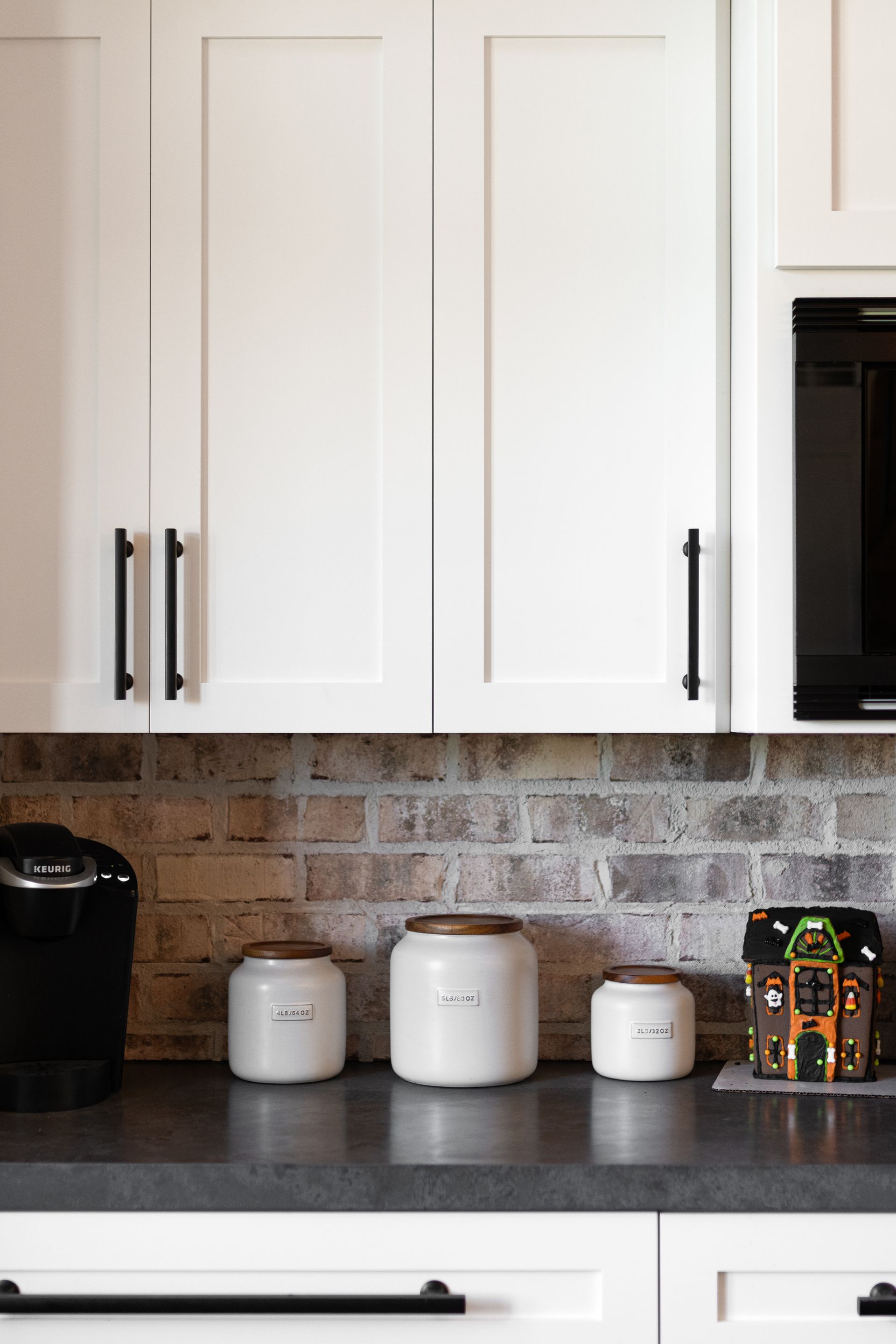 White kitchen cabinets with black hardware above a countertop with canisters and a coffee maker.