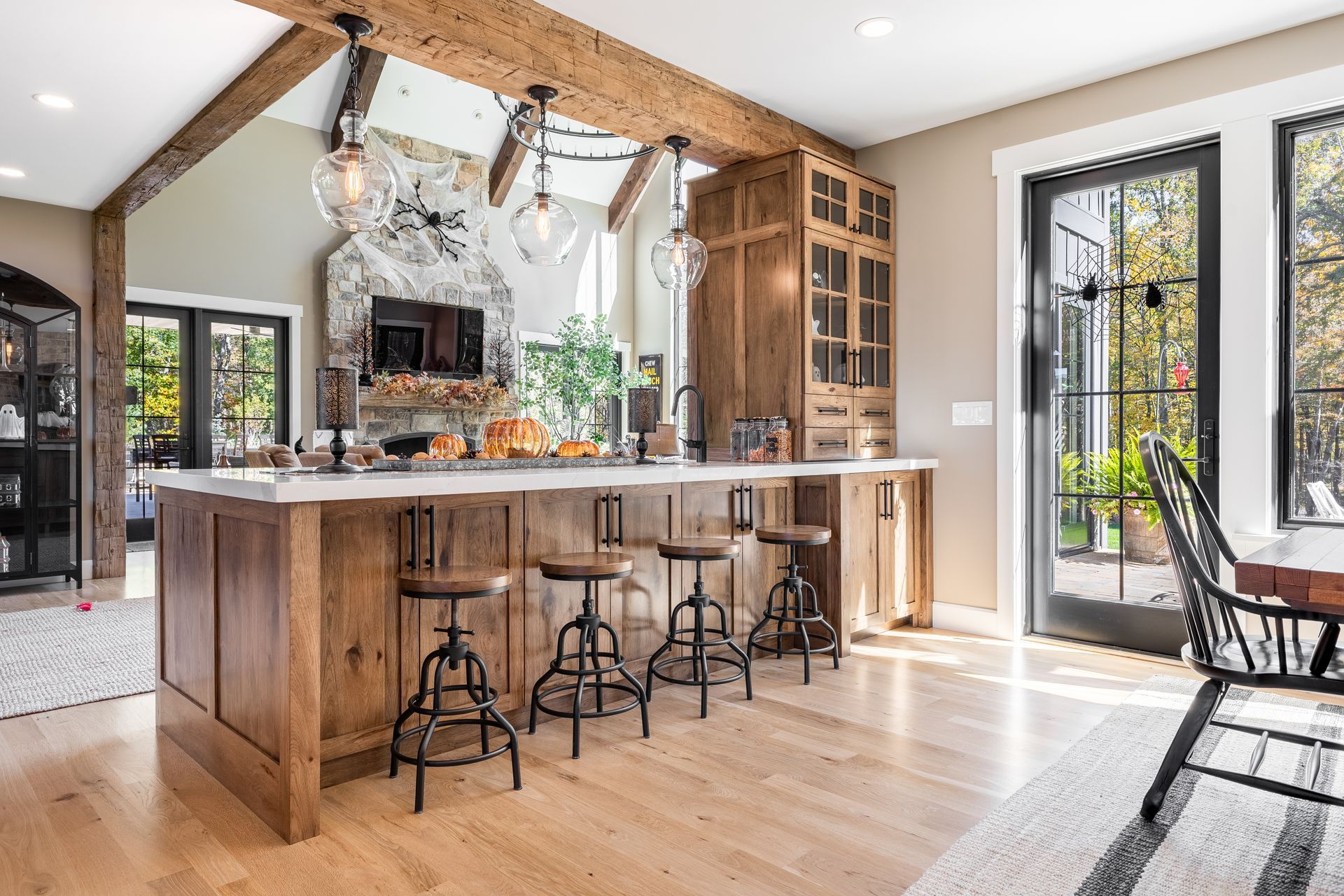 Rustic kitchen with wooden island, bar stools, and overhead lights.  Large windows offer a view outdoors.