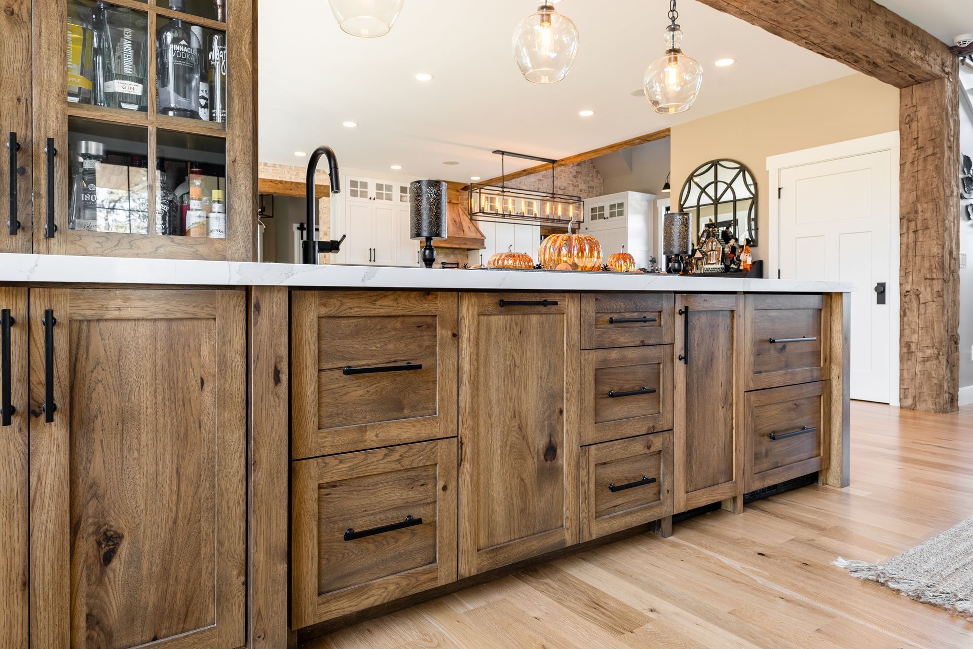 Wooden kitchen cabinets with black handles, a white countertop, and light wooden flooring.