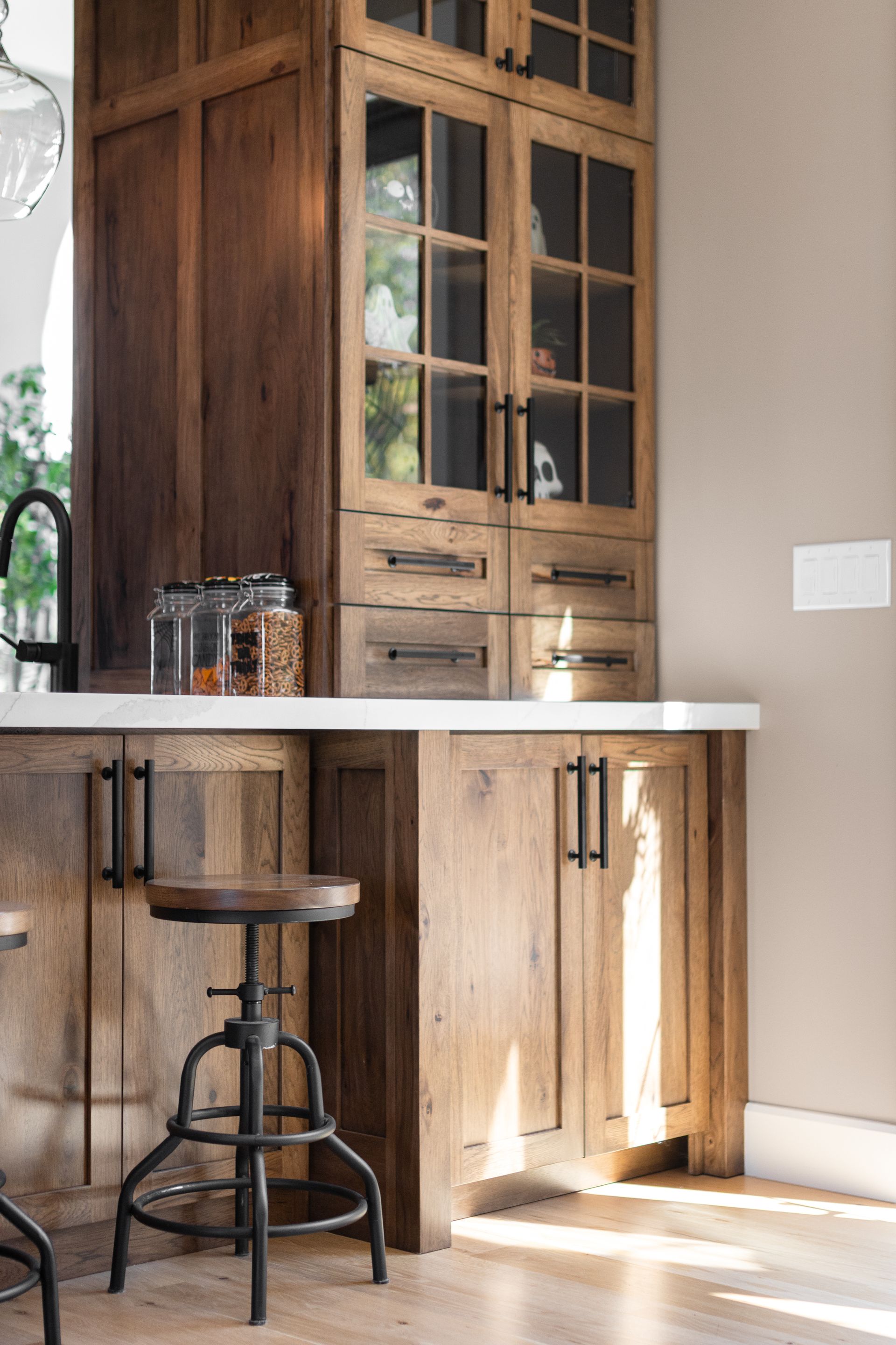 Wooden kitchen cabinets and bar with a stool, featuring glass-paned doors and a stone countertop.