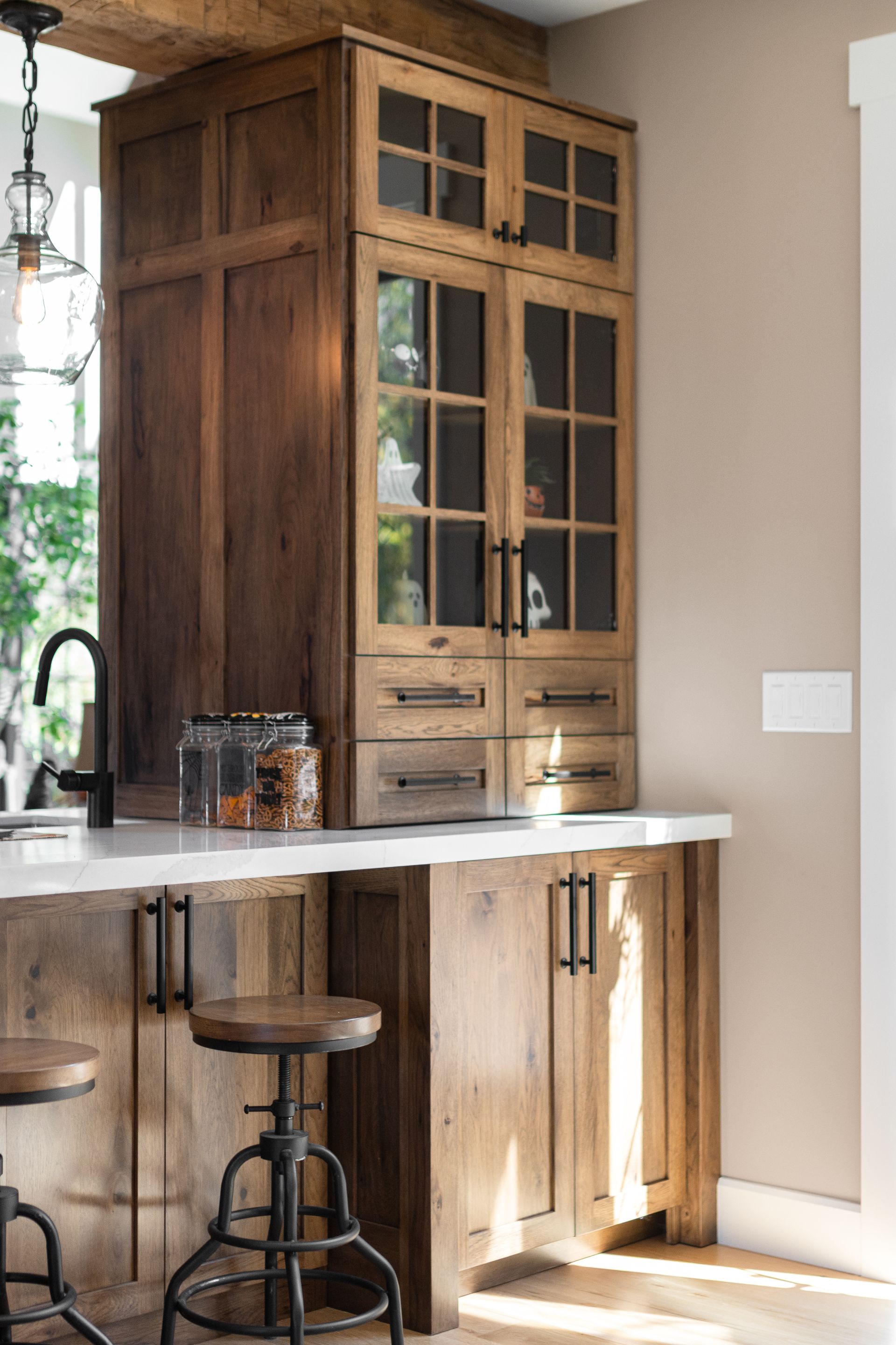 Rustic wooden kitchen cabinets with glass-front display, over a counter with a bar.