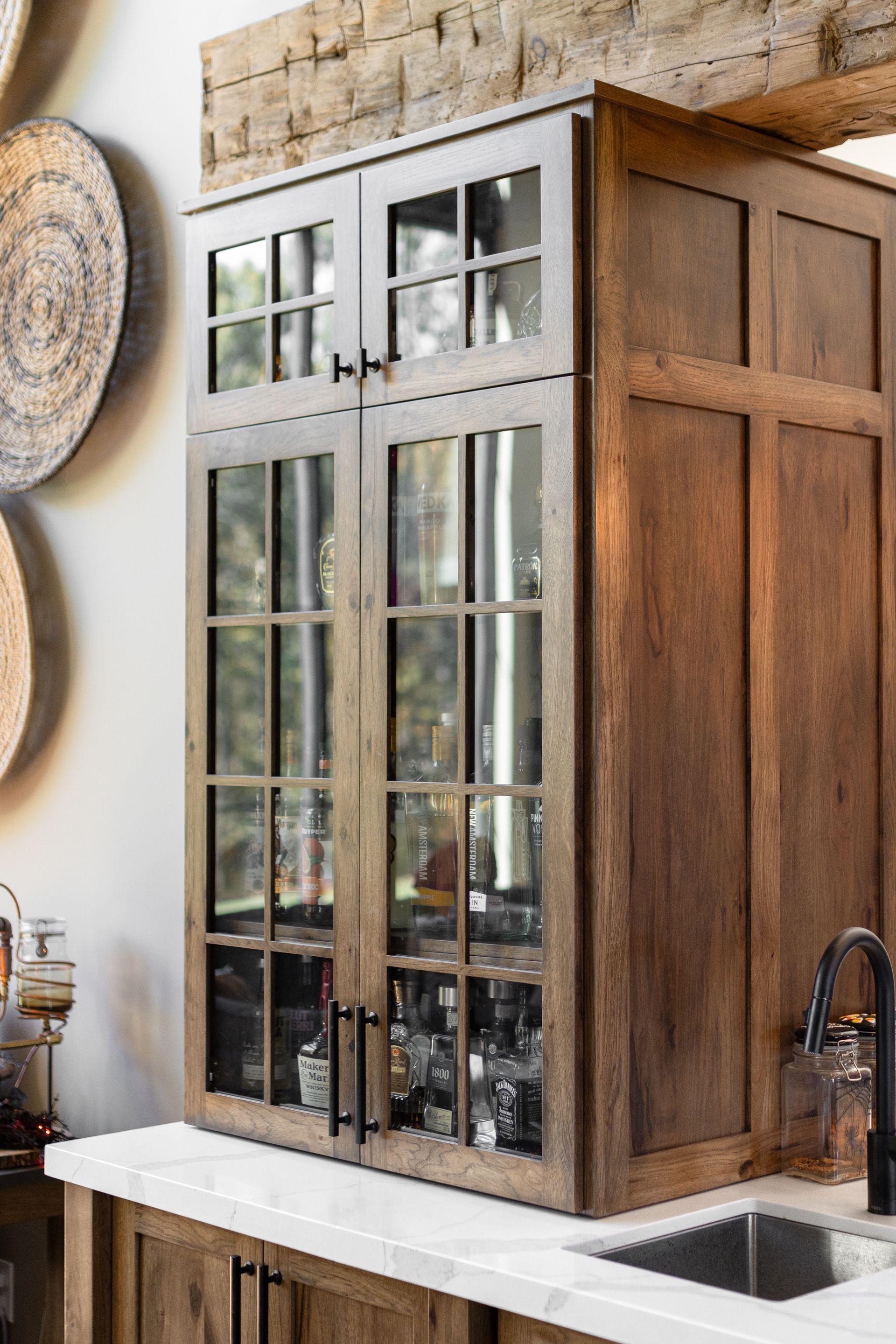 Wooden cabinet with glass-paned doors holding glassware and liquor bottles, set on a white countertop.