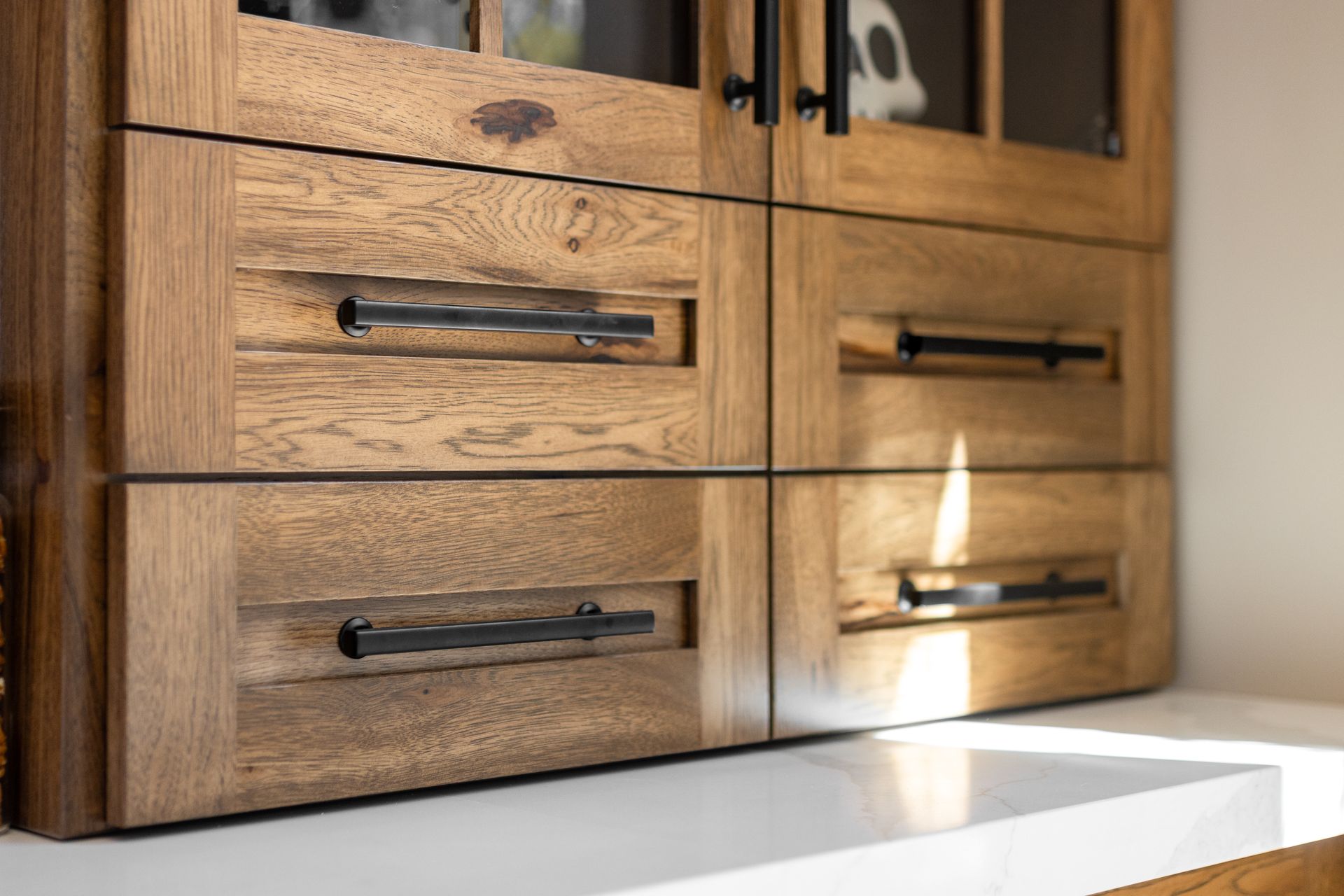 Wooden cabinet with black handles on a white counter; the cabinet features glass-paneled doors on top.