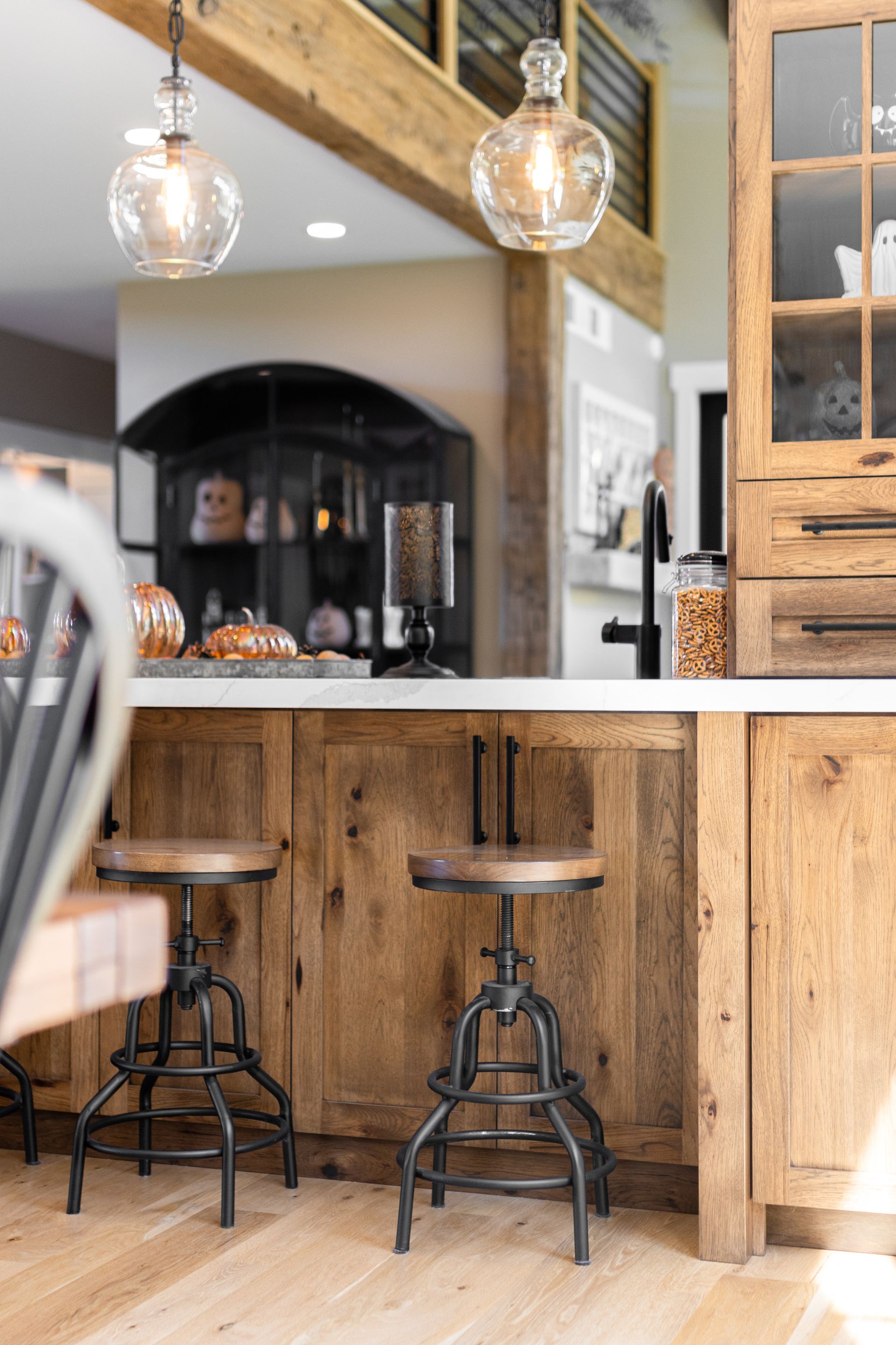 Rustic kitchen with wooden cabinets, countertop, and two metal bar stools. Two pendant lights hang overhead.