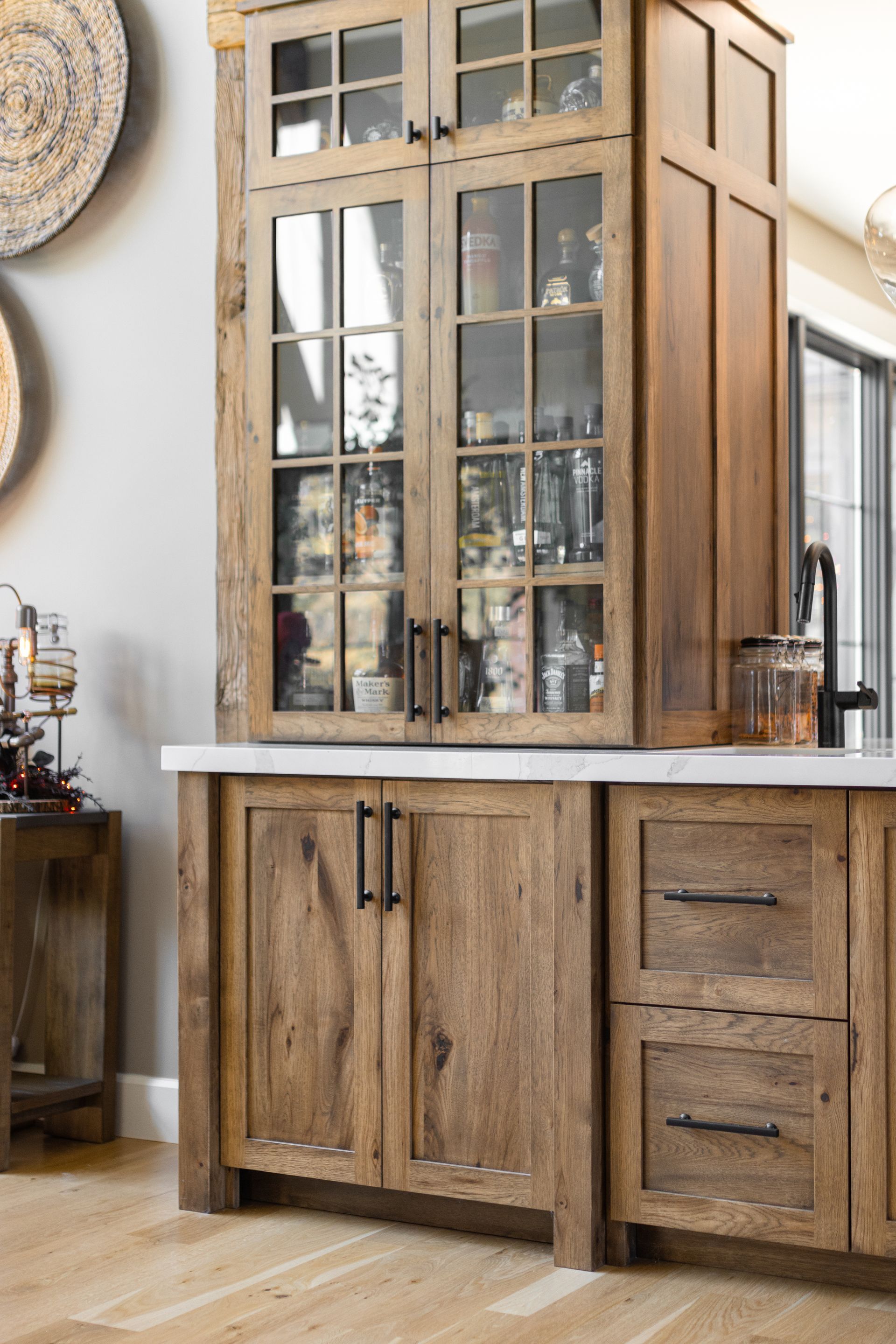 Wooden kitchen cabinet with glass-front upper doors, stone countertop, and dark hardware.