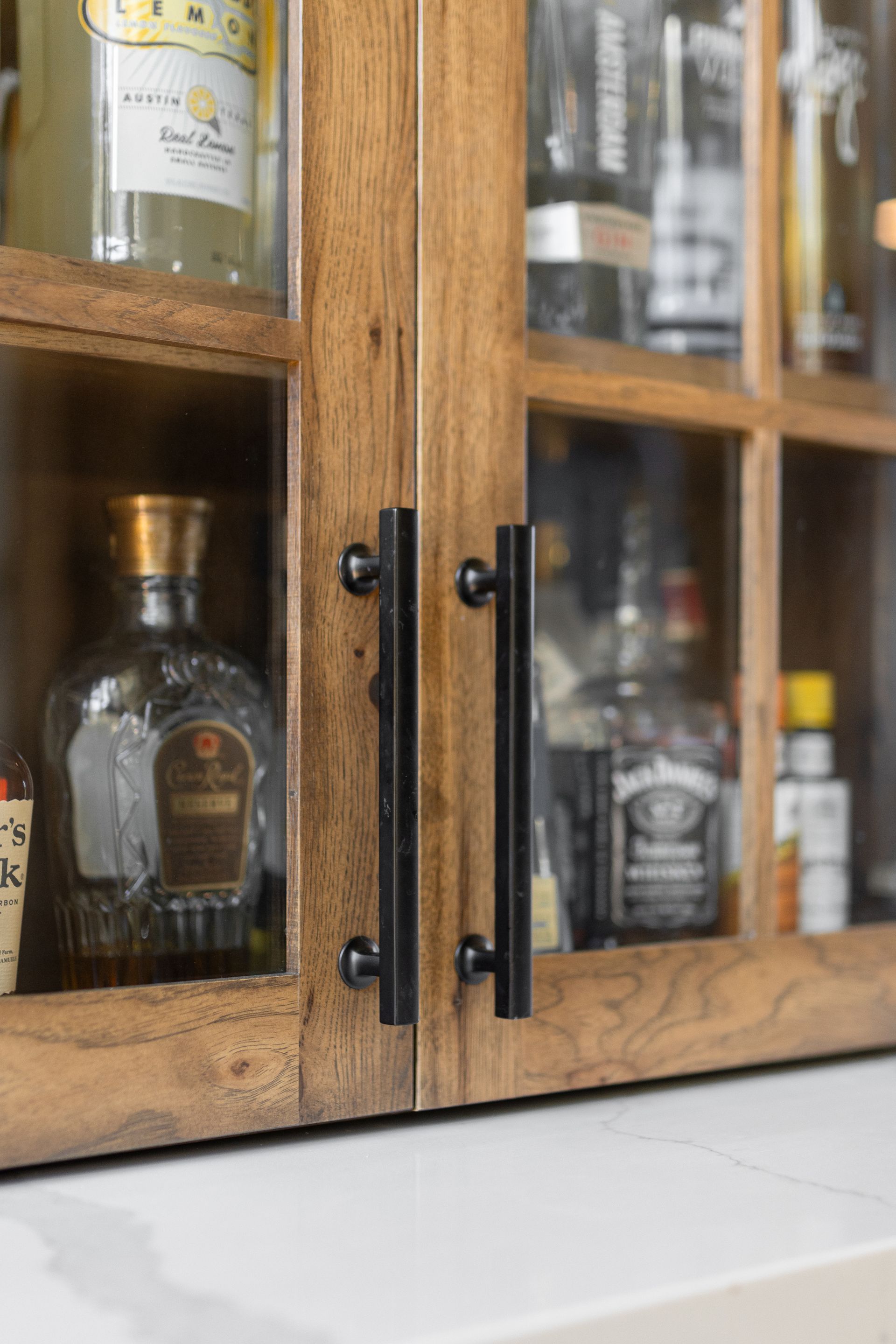 Wooden cabinet doors with black handles, displaying liquor bottles on a white countertop.