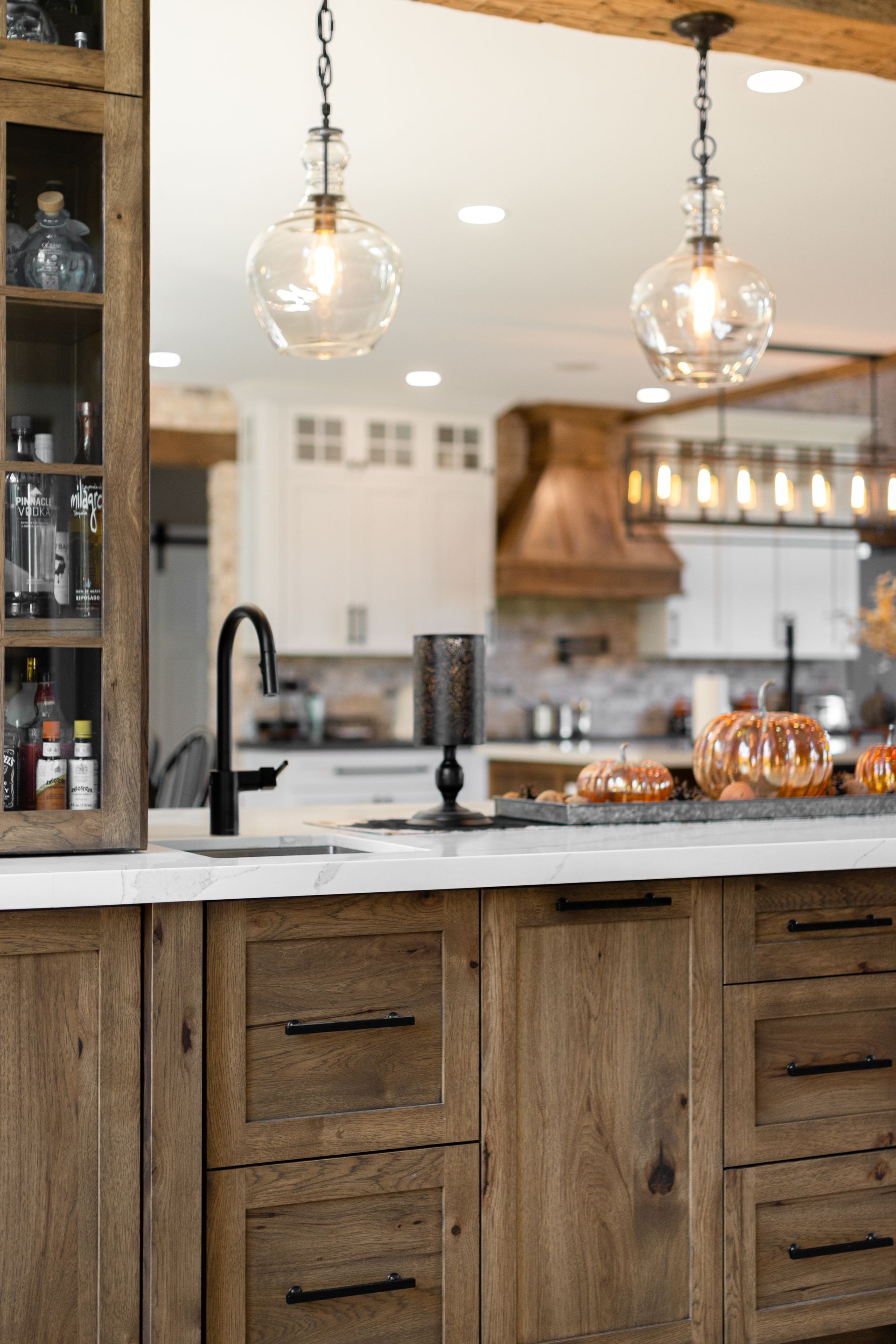 Rustic kitchen with wood cabinetry, black faucet, pendant lights, and island.
