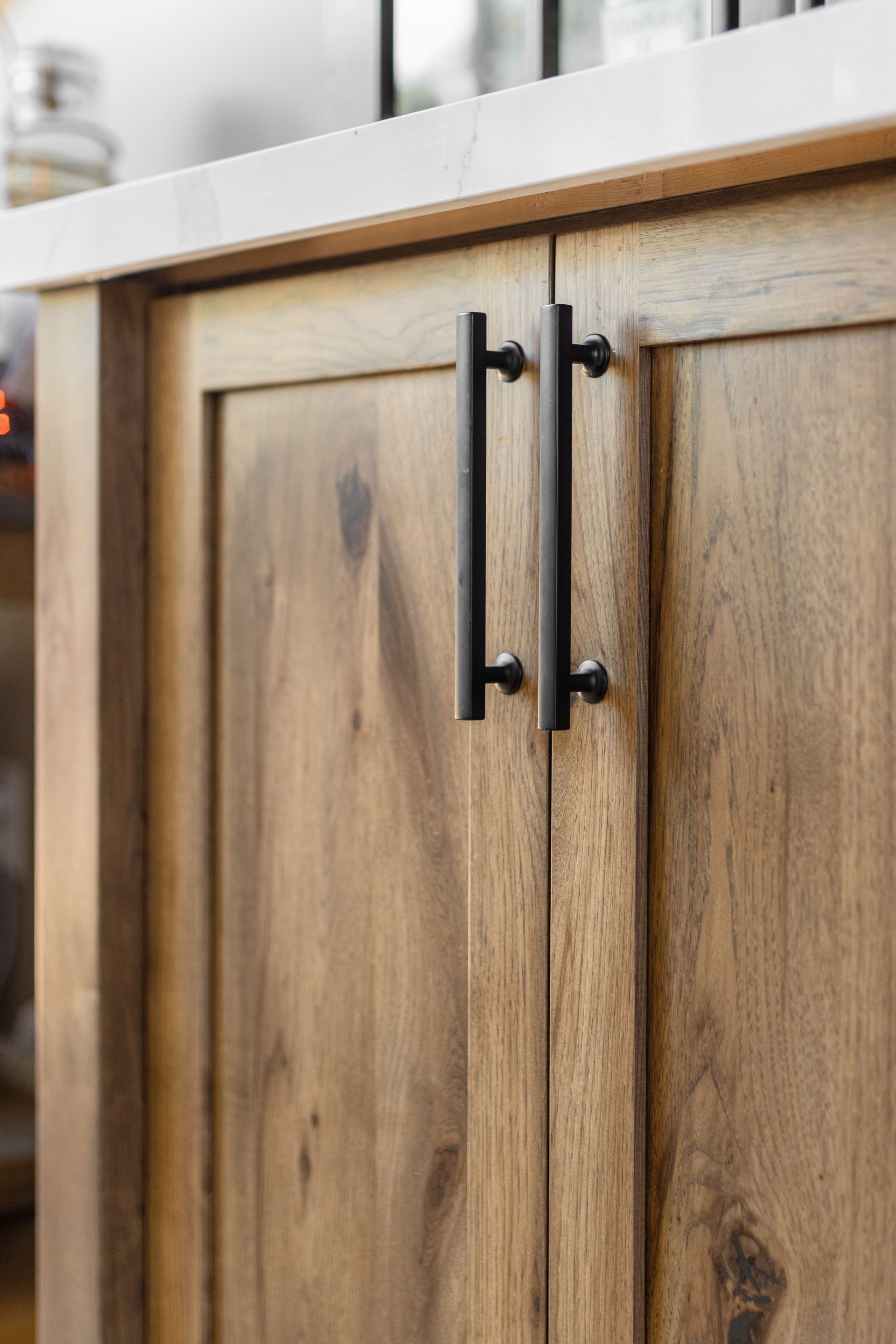 Wooden cabinet doors with black handles, a white countertop, and natural wood grain.
