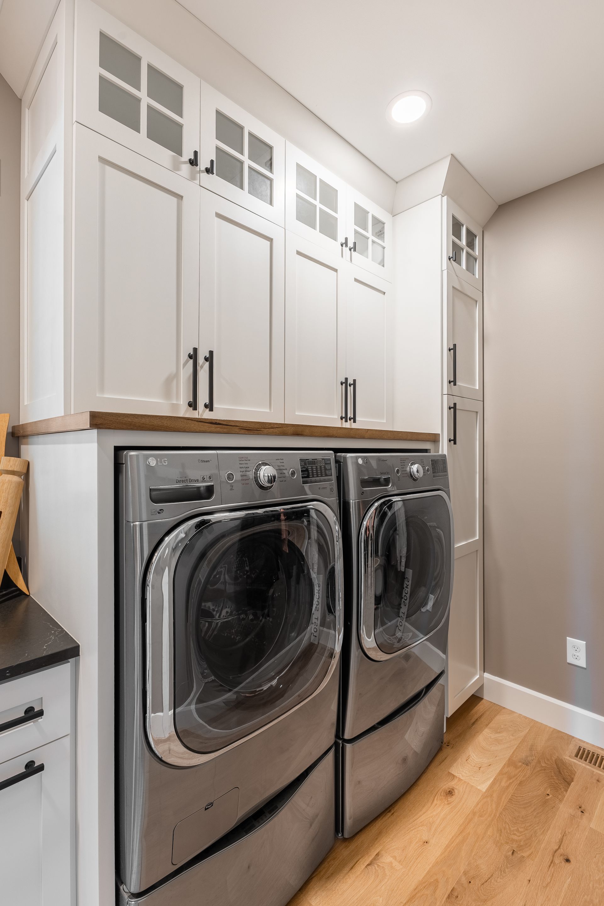 A laundry room with a silver washer and dryer, white cabinets, and wood flooring.
