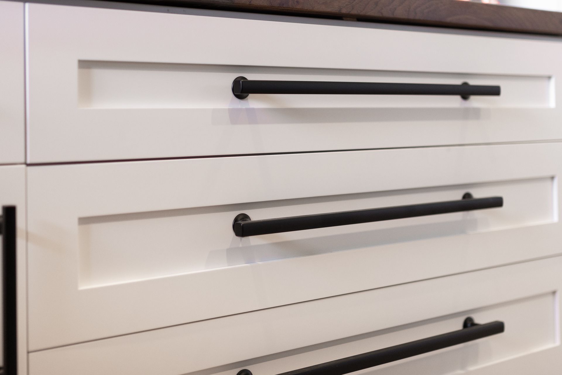 White kitchen cabinet drawers with black bar handles.