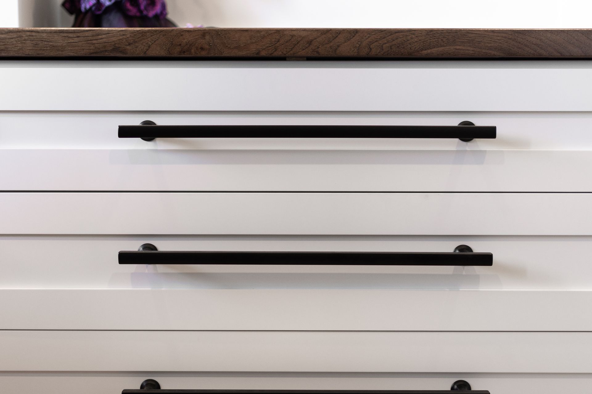 White kitchen drawers with black bar handles beneath a dark wooden countertop.