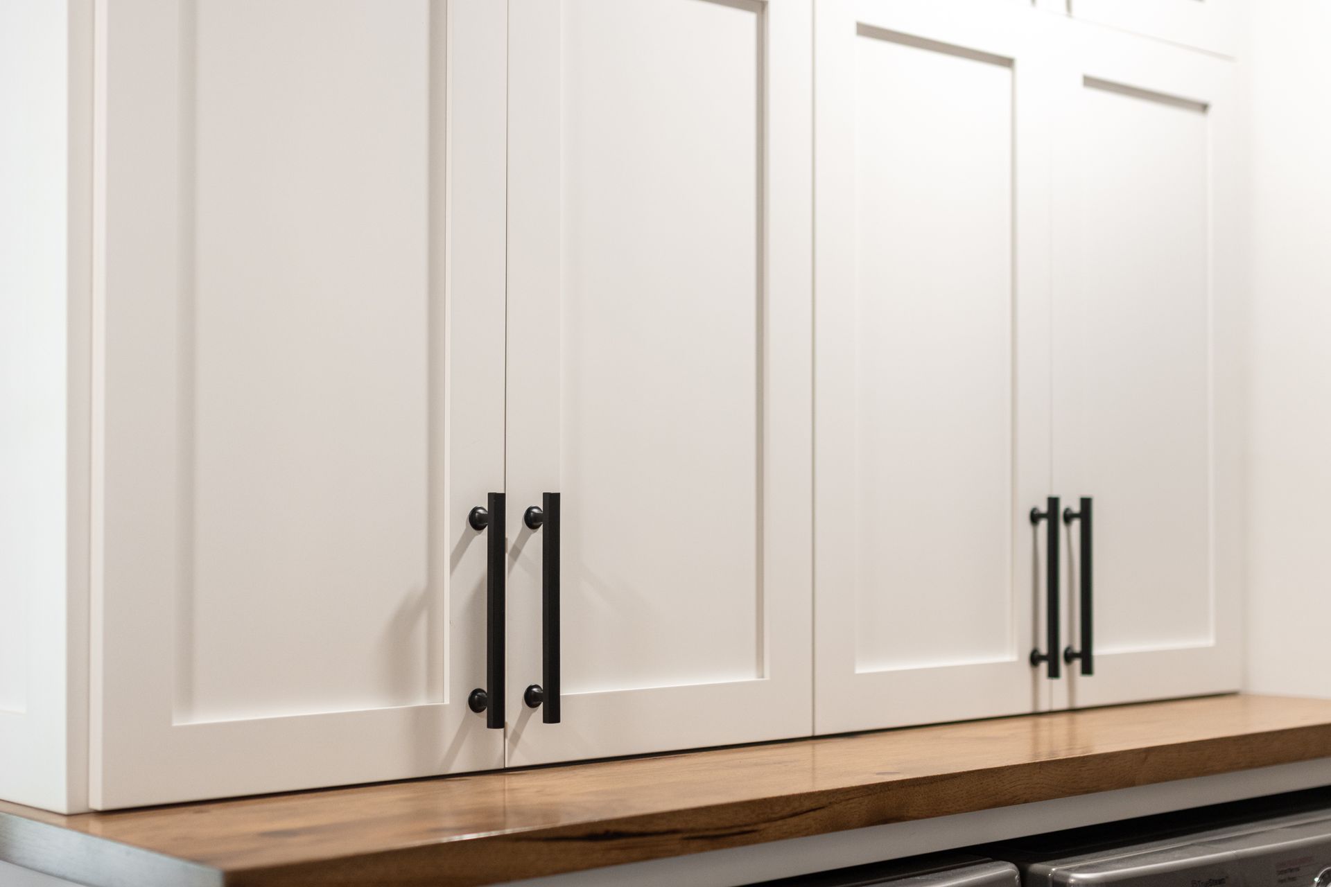 White cabinets with black handles above a wooden countertop.