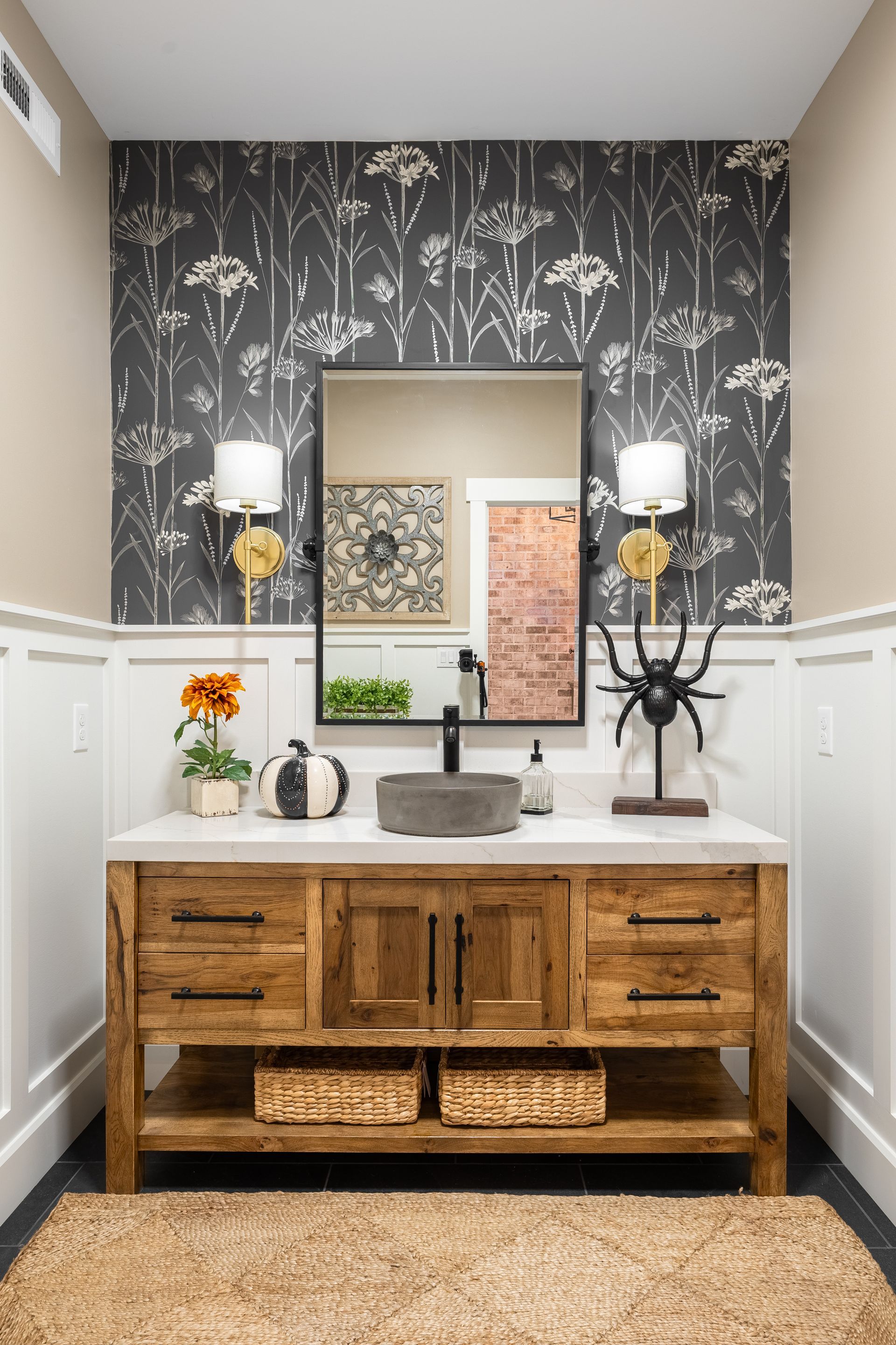 Bathroom with wooden vanity, patterned wallpaper, large mirror, and Halloween decorations.