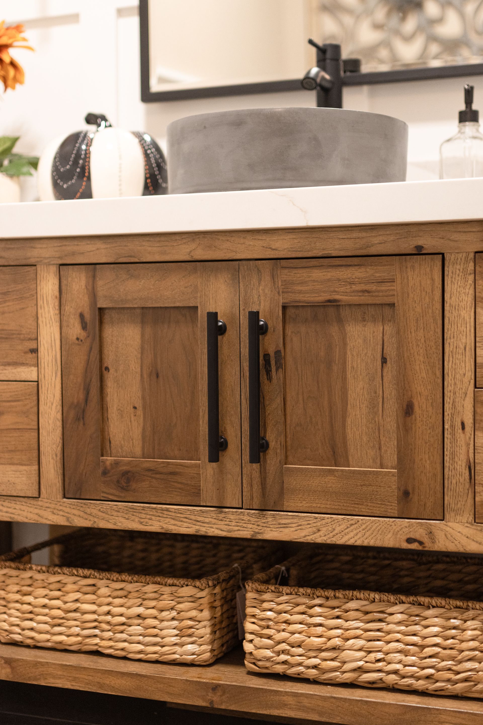 Wooden bathroom vanity with black hardware, stone sink, and woven baskets.