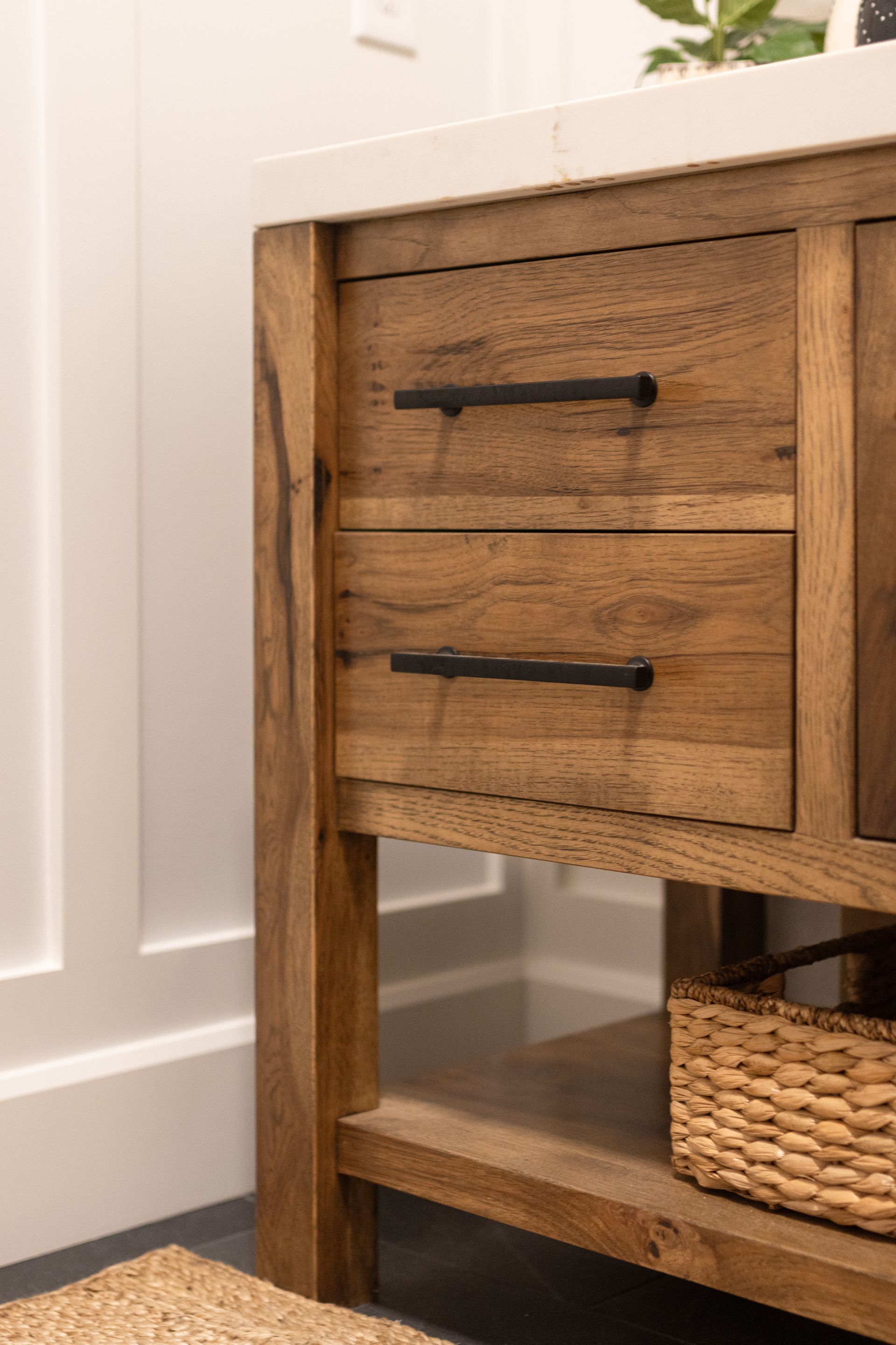 Wooden bathroom vanity with black handles, two drawers, and a woven basket.