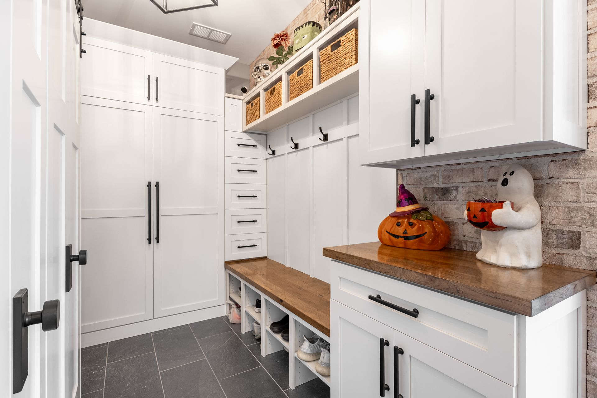 White mudroom with cabinets, bench, and Halloween decorations.